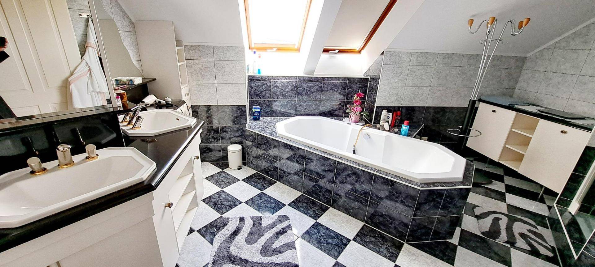 Geräumiges Badezimmer mit Badewanne, Doppelwaschbecken und schwarz-weiß kariertem Fliesenboden.