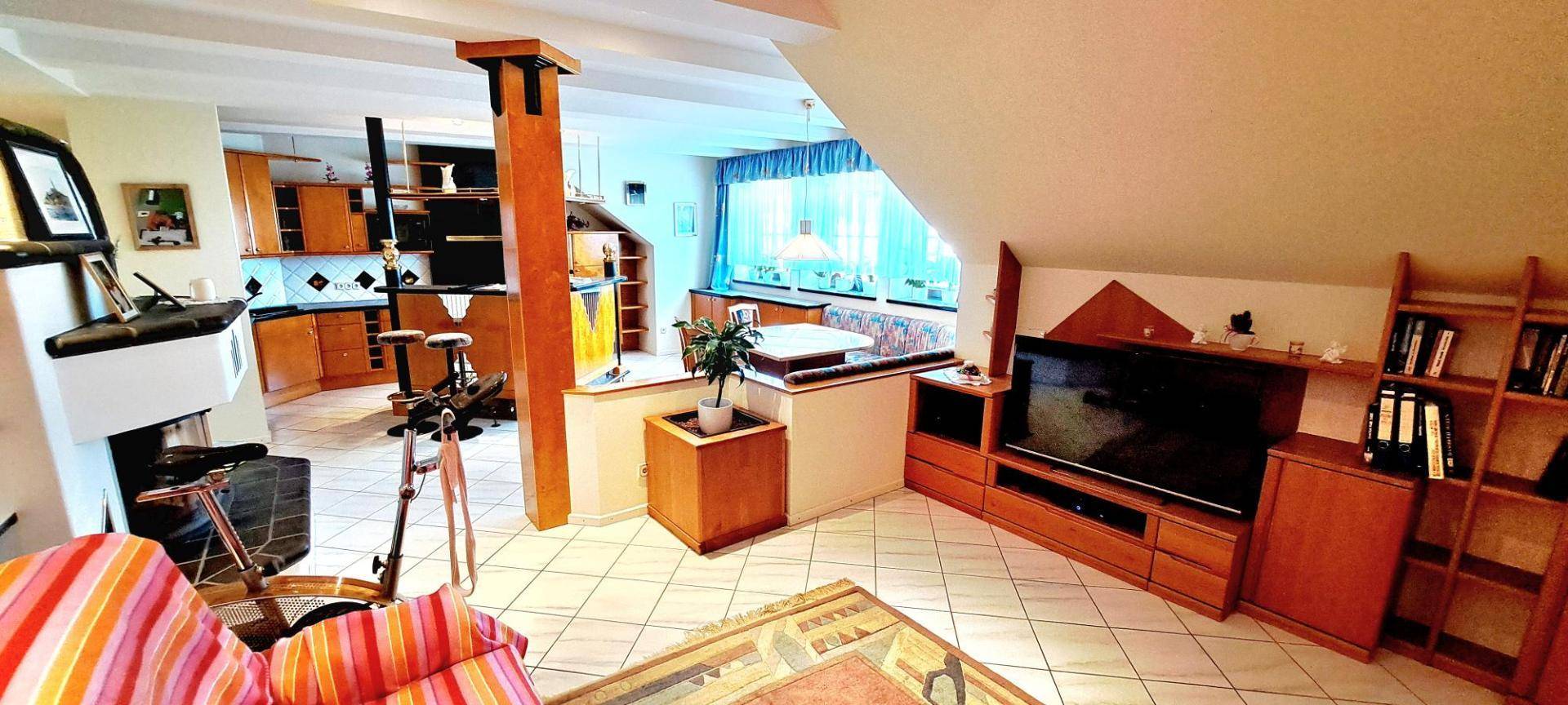 Offener Wohn- und Essbereich mit Fliesenboden, Fernseher und Holzmöbeln.