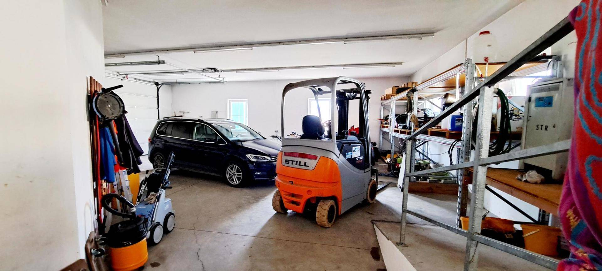 Geräumige Garage mit Platz für Fahrzeuge, Gabelstapler und Lagerregale.