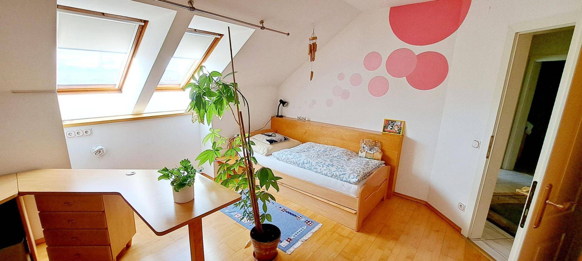 Helles Schlafzimmer im Dachgeschoss mit Einzelbett, Schreibtisch und Dachfenstern.