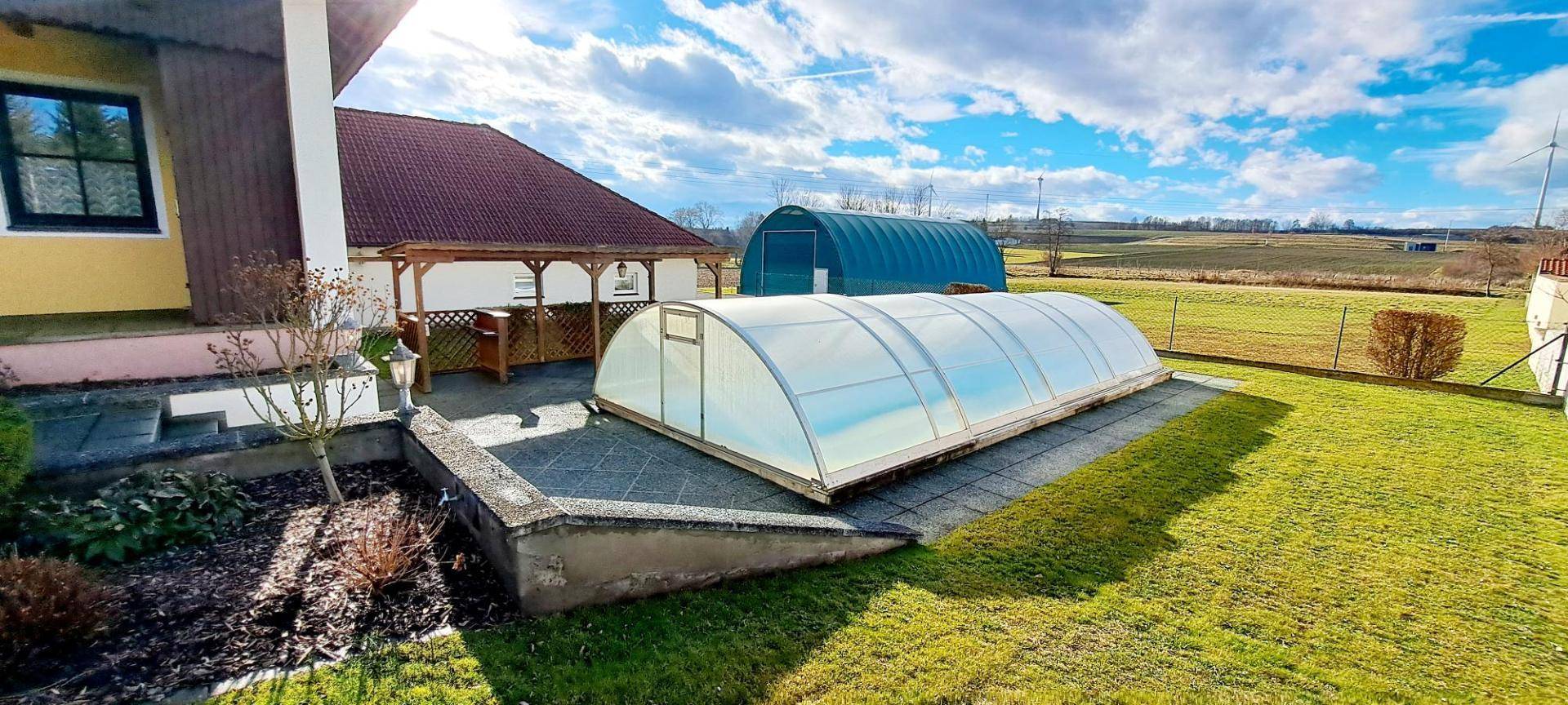 Gepflegter Gartenbereich mit überdachtem Pool und Blick auf die weite Landschaft.