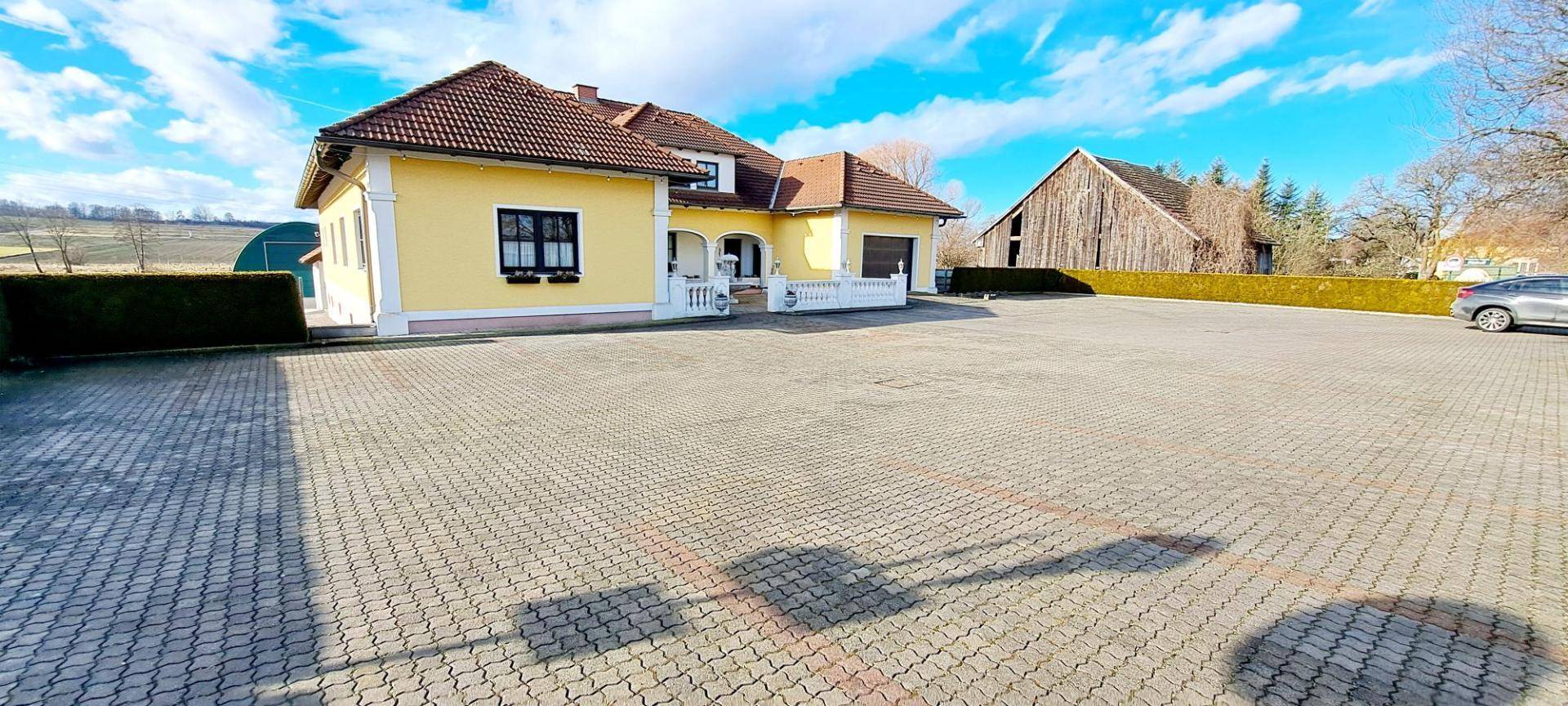 Weitläufiger Vorplatz vor dem Landhaus mit angrenzendem Feld und Scheune im Hintergrund.
