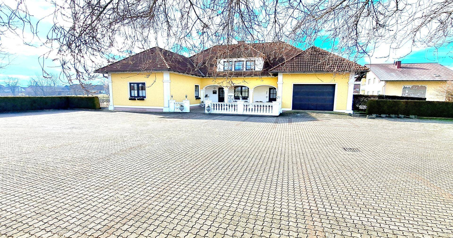 Vorderansicht des Landhauses mit großem gepflastertem Vorplatz und Eingangsbereich.