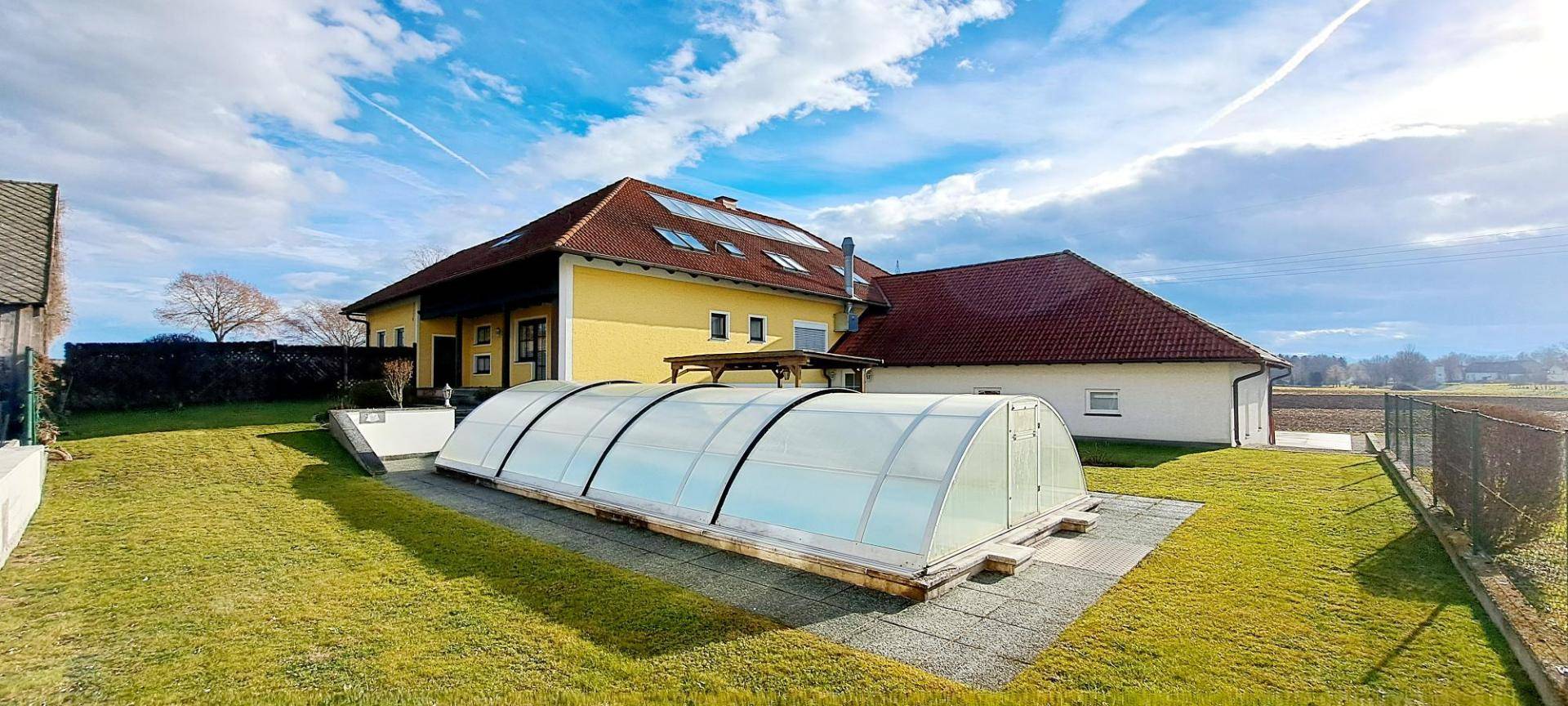 Großzügiger Gartenbereich mit überdachtem Pool und Blick auf die umliegende Landschaft.