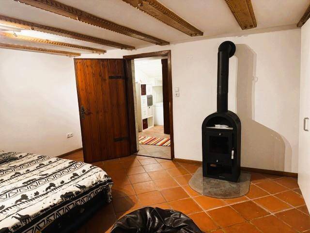 Schlafzimmer mit Holzbalkendecke, Terrakottaboden und einem gemütlichen Holzofen.