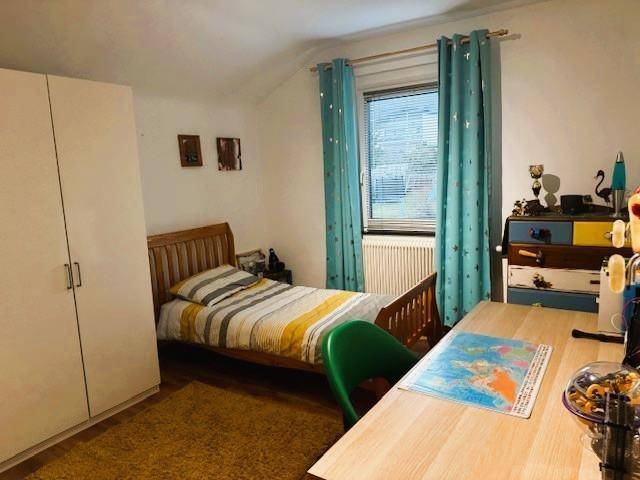 Kinderzimmer mit Einzelbett, Schreibtisch und bunten Vorhängen, hell und freundlich gestaltet.