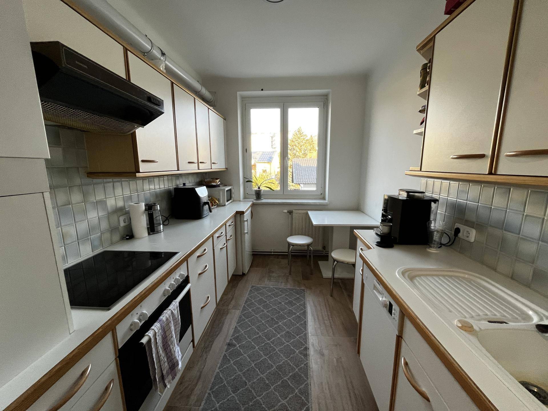 Helle Küche mit Fenster, weißen Schränken, Essbereich und modernen Geräten.