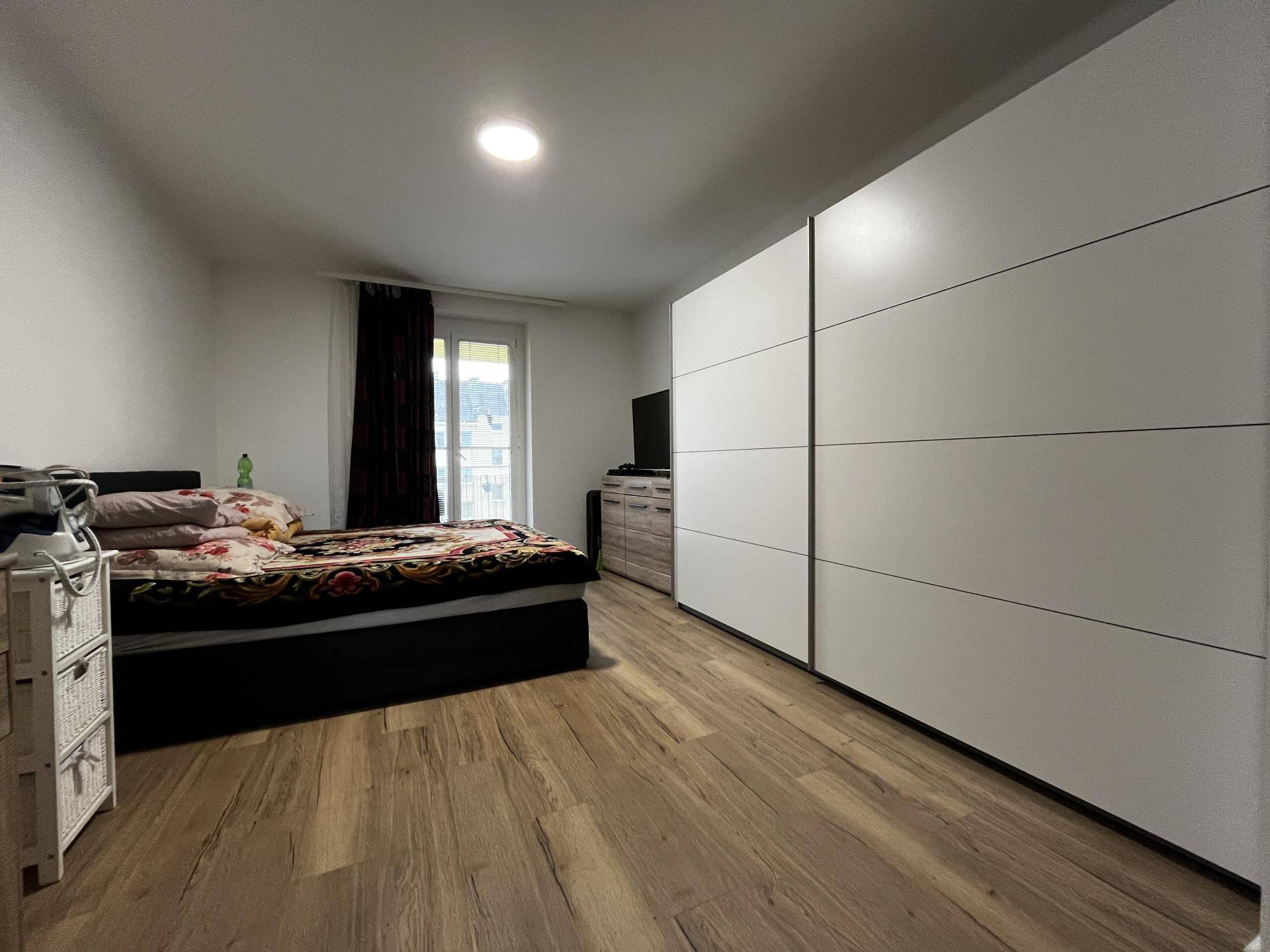Helles Schlafzimmer mit Doppelbett, großem weißen Kleiderschrank und Balkonzugang.