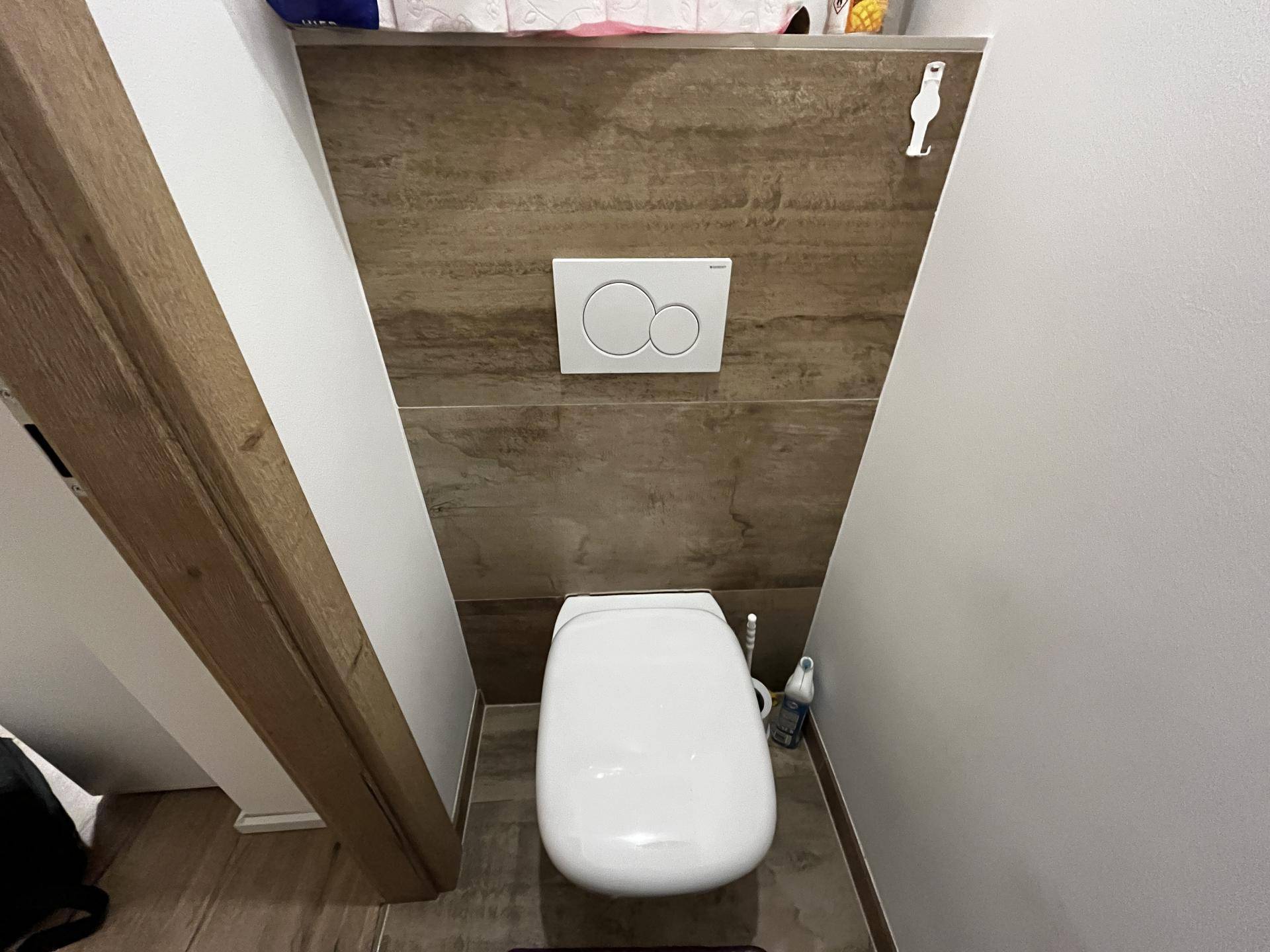 Separate Toilette mit Wand-WC und Fliesen an der Wand, unter einer Dachschräge.