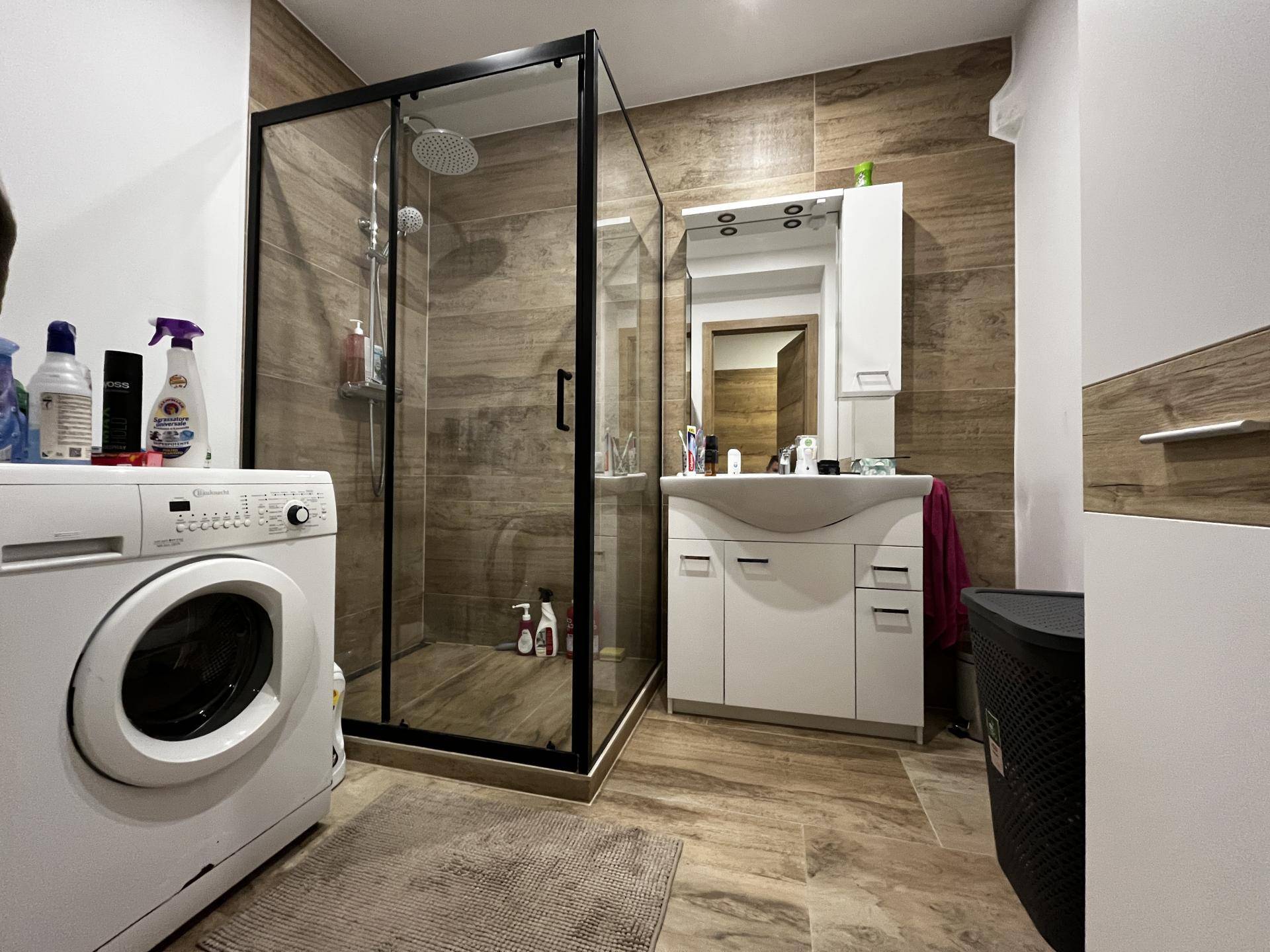 Modernes Badezimmer mit begehbarer Dusche, Waschbecken und Waschmaschine.