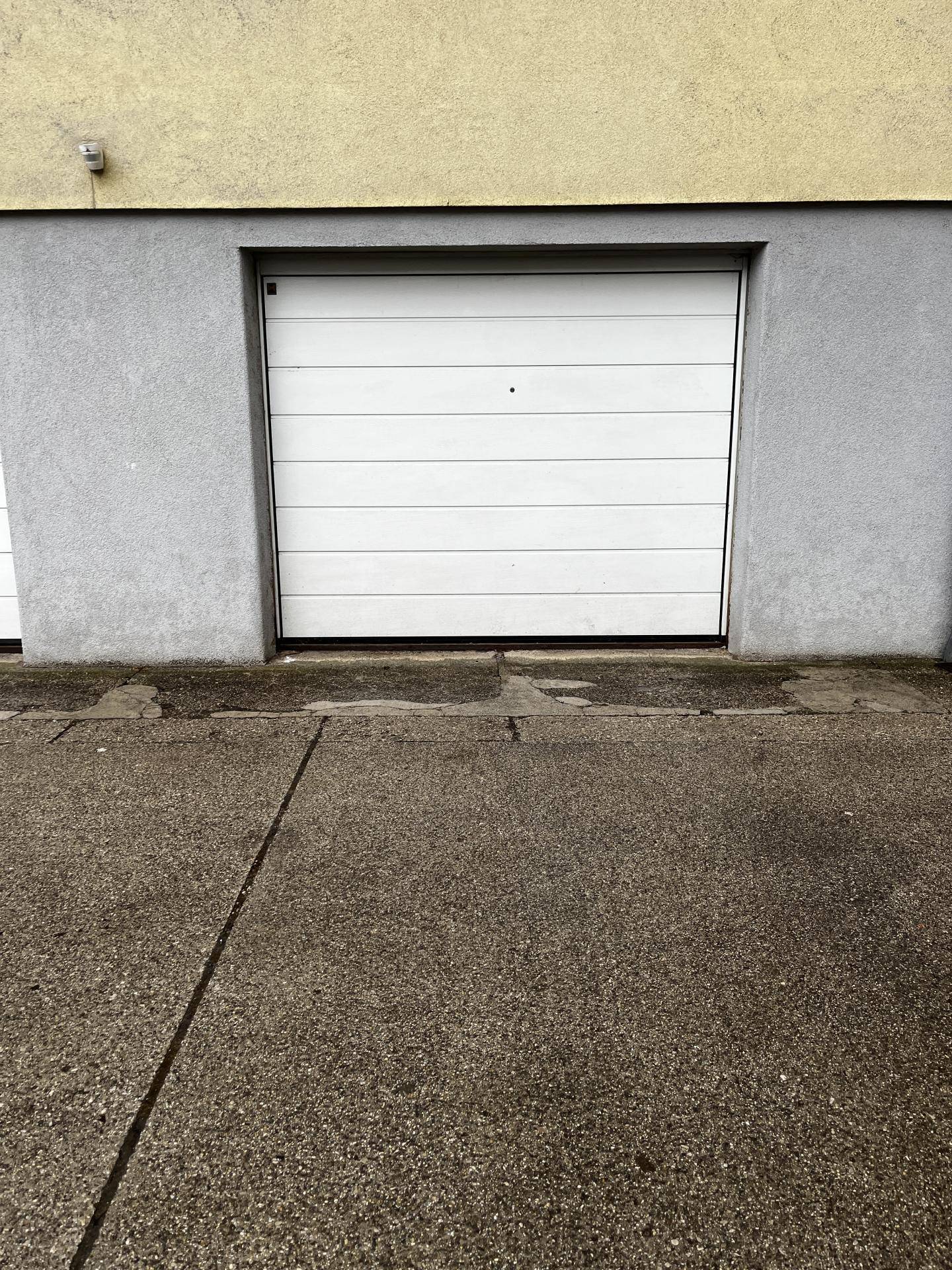 Weiße Garagentür in einer grauen Fassade mit Betonboden davor.