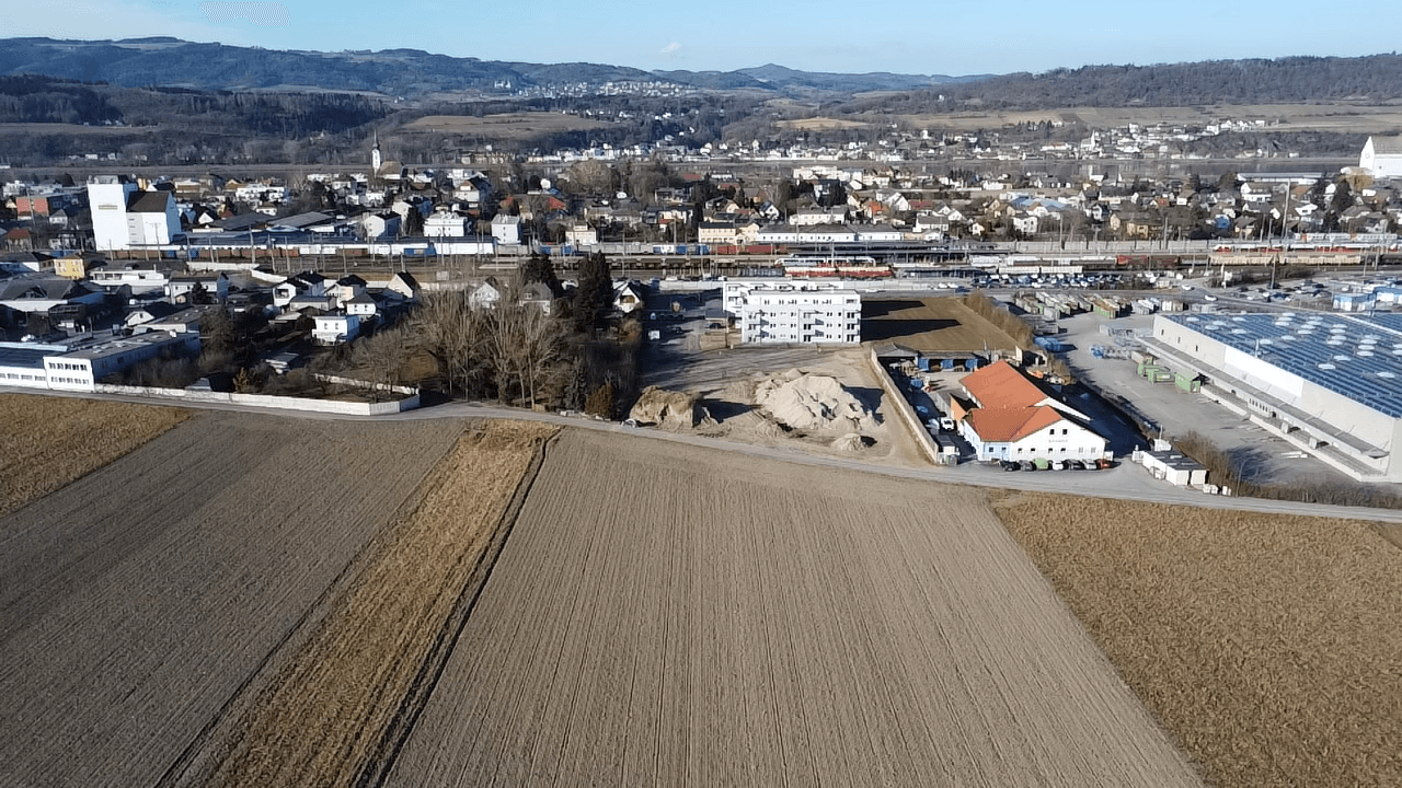 Luftaufnahme einer ländlichen Gegend mit angrenzendem Industriegebiet und Wohnsiedlung im Hintergrund.