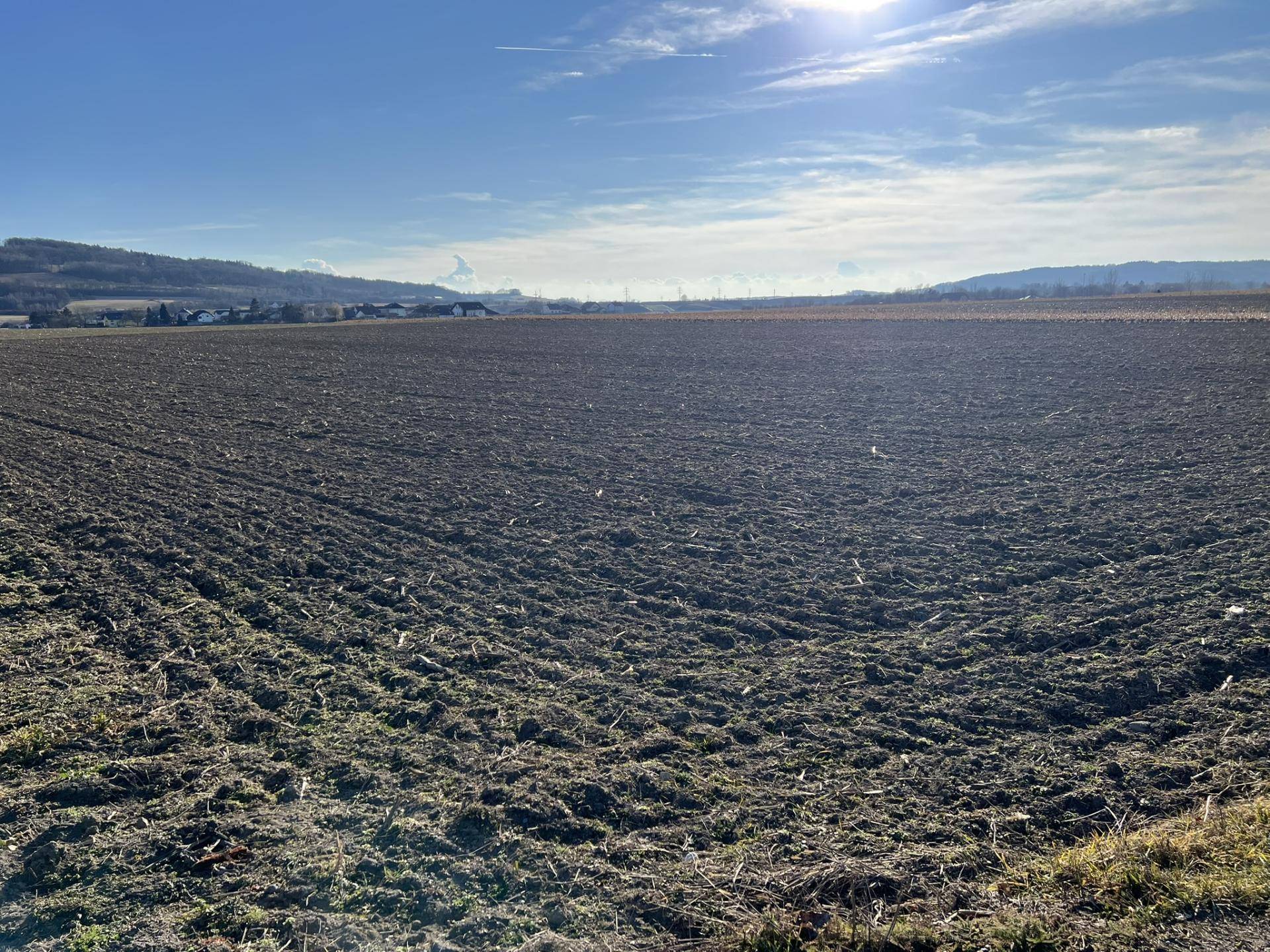 Weites, frisch gepflügtes Feld unter einem strahlend blauen Himmel mit heller Sonne.