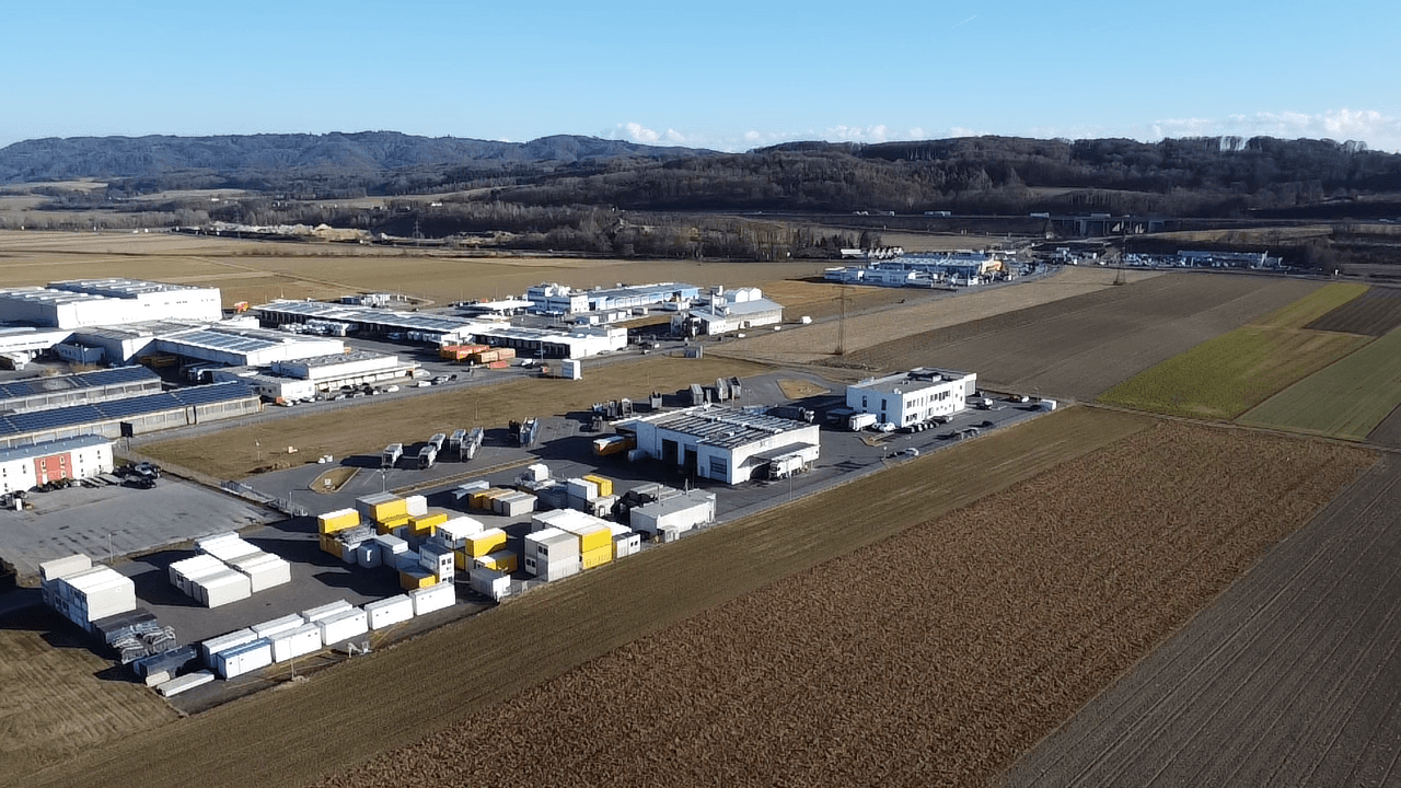 Luftaufnahme eines Industriegebiets mit verschiedenen Gebäuden, Containern und weiten Feldern.