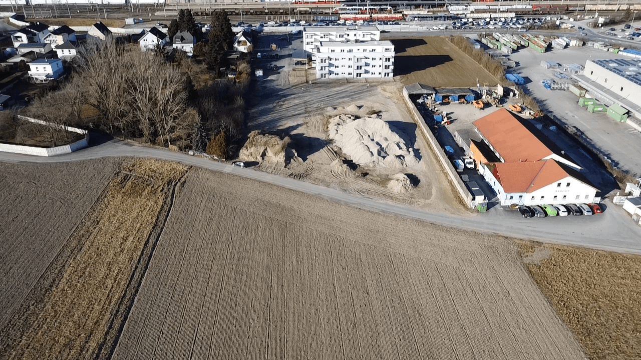 Luftaufnahme einer ländlichen Gegend mit angrenzendem Industriegebiet und Wohnsiedlung im Hintergrund.