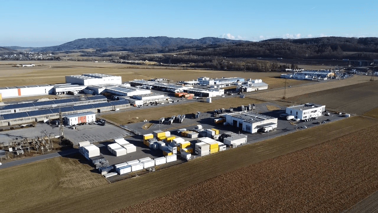 Luftaufnahme eines ausgedehnten Industriegebiets mit Lagerhallen und weiten Feldern im Vordergrund.