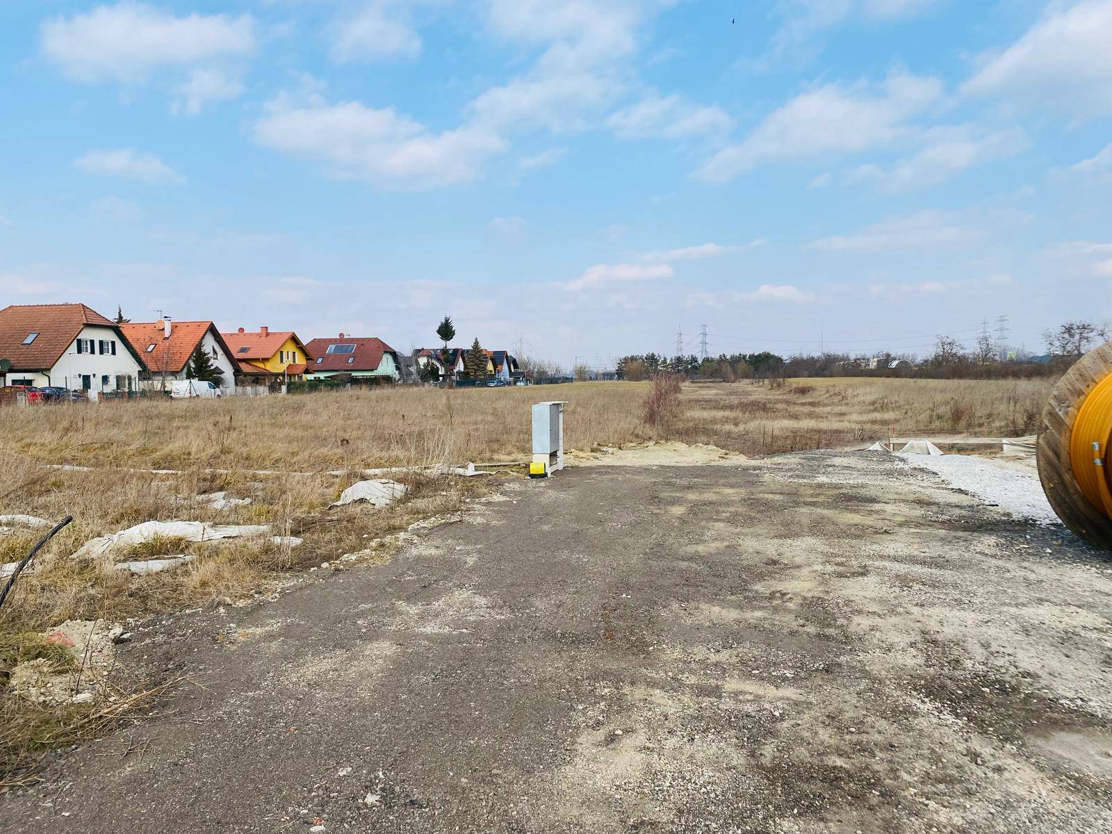 Weitläufiges Baugrundstück mit trockenem Gras, umgeben von Wohnhäusern und offener Landschaft.
