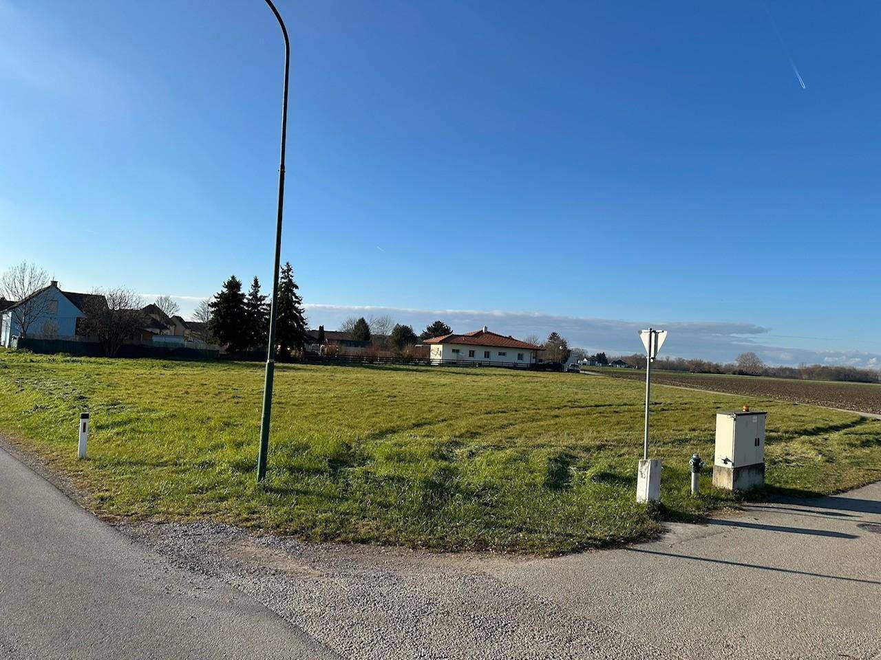 Offenes Grundstück mit grüner Wiese und ländlicher Umgebung unter strahlend blauem Himmel.