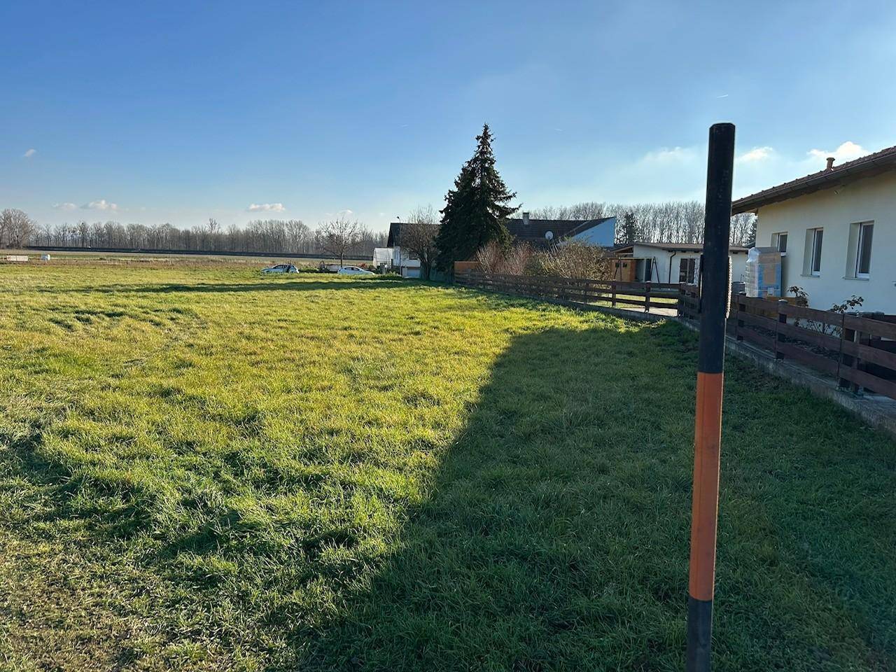 Grüne Wiese eines Grundstücks mit angrenzendem Zaun und Wohnhaus im ländlichen Umfeld.