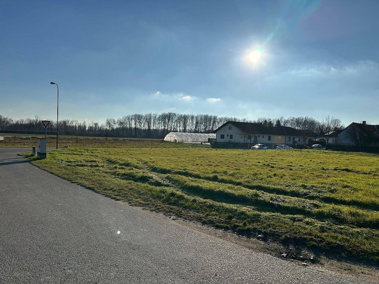 Sonniges Grundstück mit weitem Blick über grüne Wiesen und angrenzende Bebauung mit Gewächshaus.