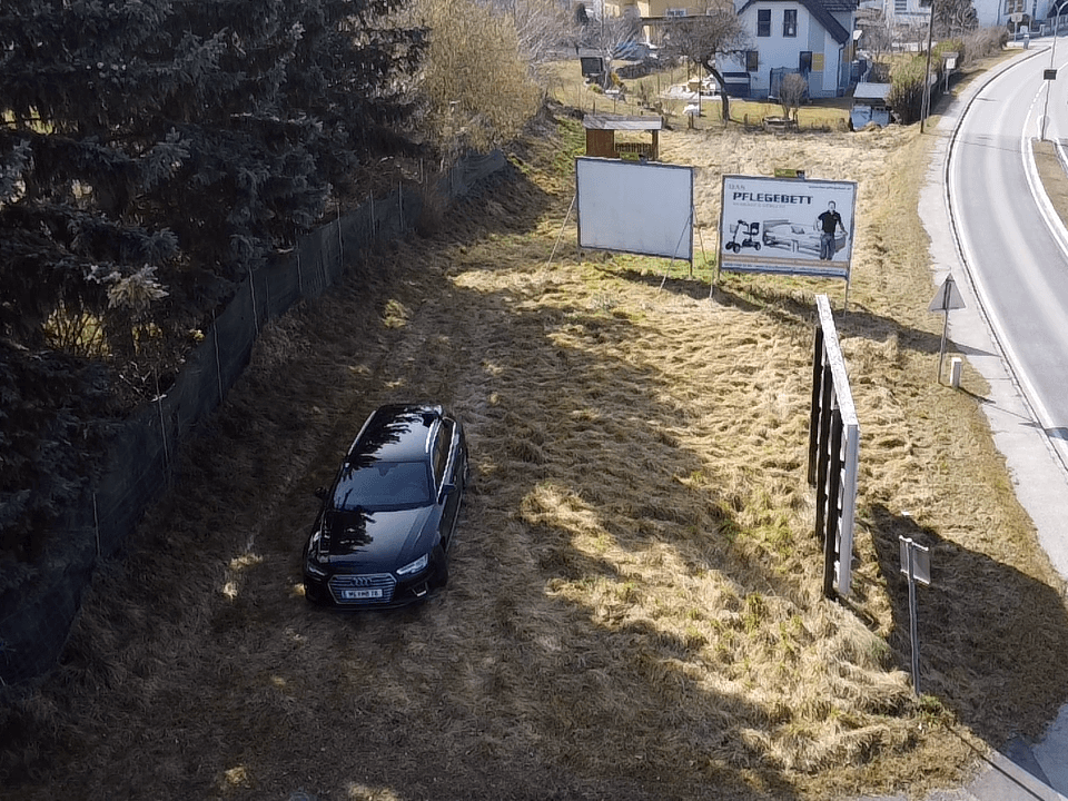 Luftaufnahme des Grundstücks mit einem schwarzen Auto auf dem Gras und mehreren Werbetafeln entlang der Straße.