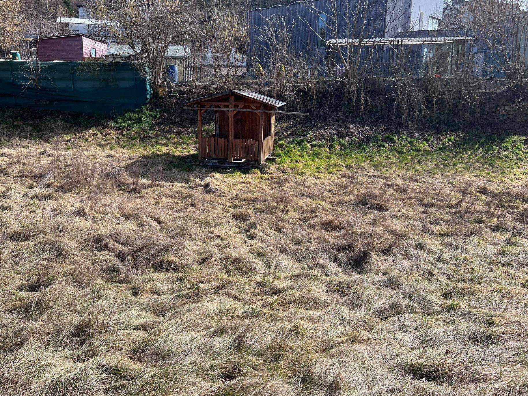 Nahaufnahme des rustikalen Holzpavillons auf dem grasbewachsenen Grundstück, umgeben von natürlicher Vegetation.