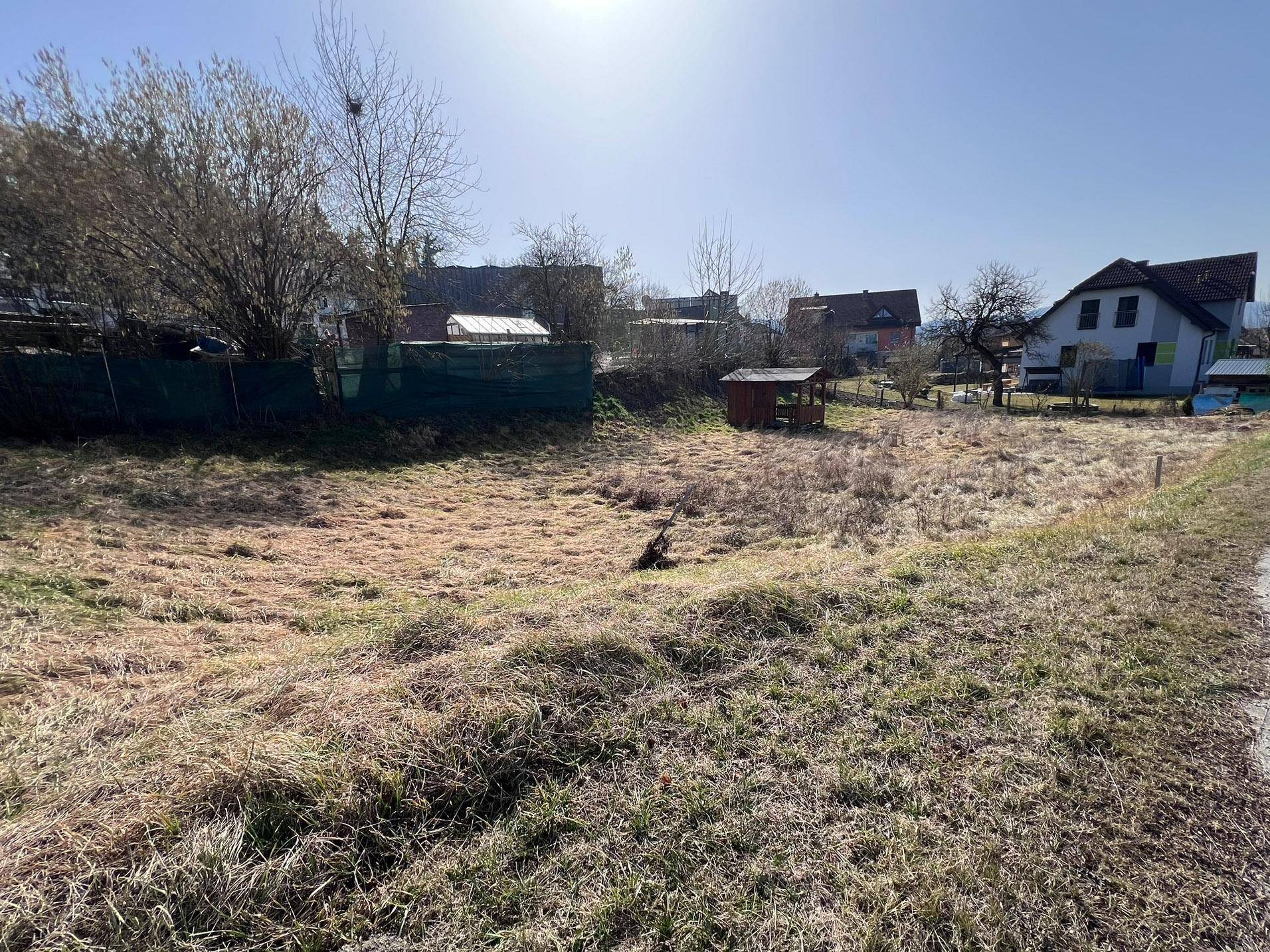 Weitläufiges, grasbewachsenes Grundstück mit einem kleinen Holzpavillon im hinteren Bereich unter klarem Himmel.
