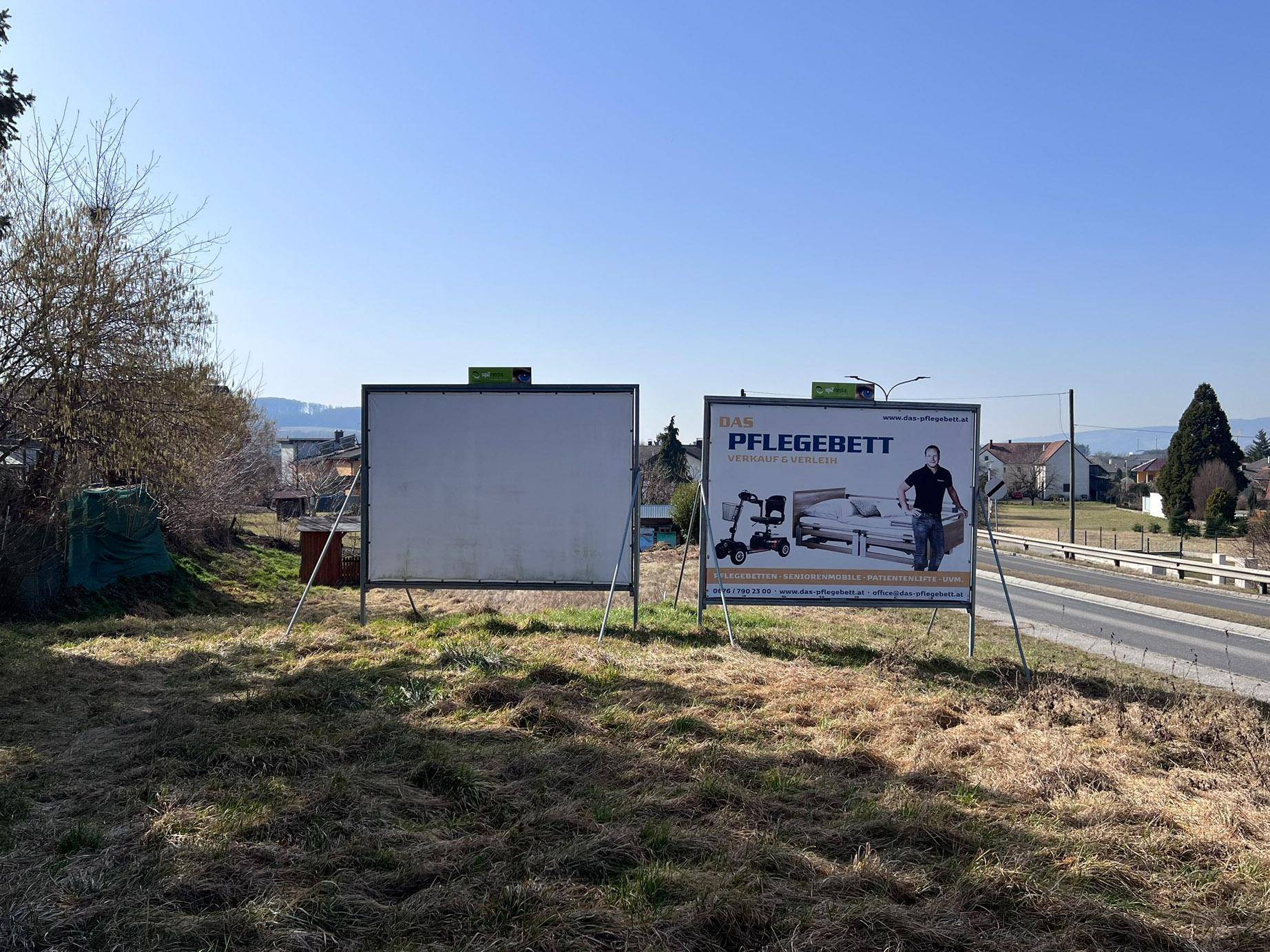 Bodennahe Ansicht des Grundstücks mit zwei großen Werbetafeln und der angrenzenden Straße unter blauem Himmel.