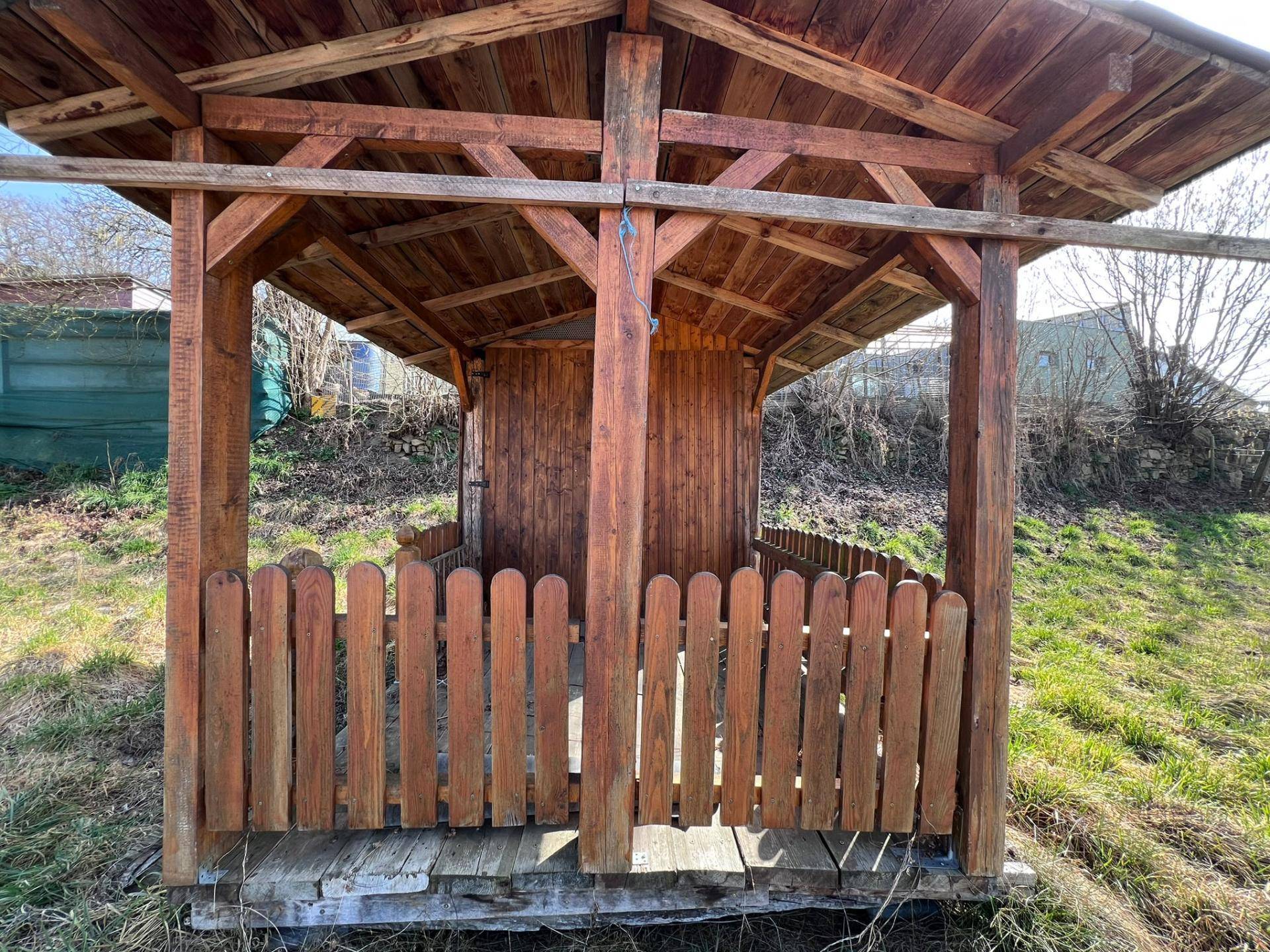 Detaillierte Ansicht des hölzernen Pavillons mit seiner robusten Konstruktion und dem Lattenzaun.