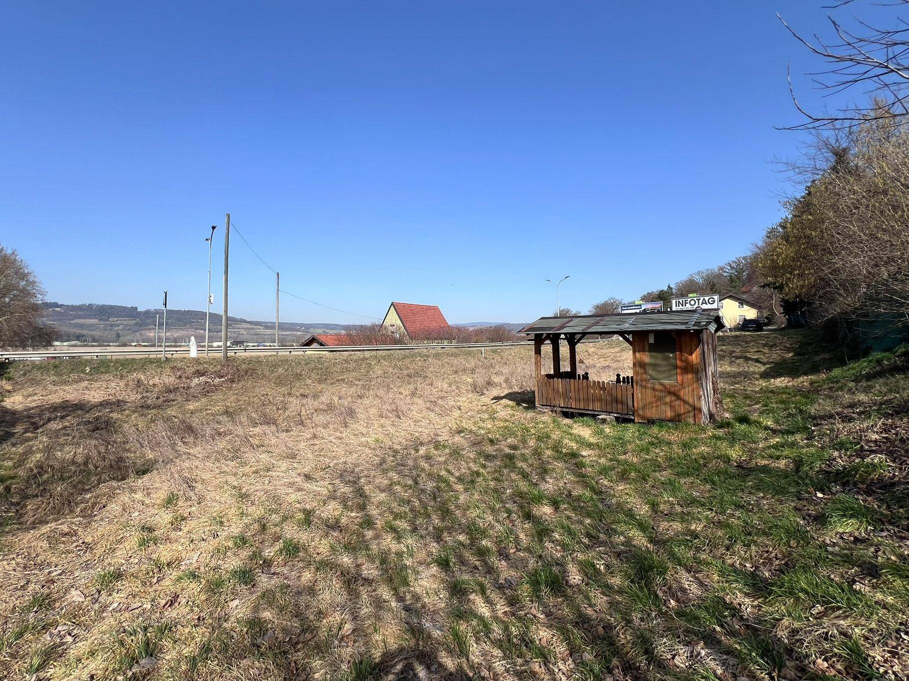 Blick vom Holzpavillon über das Grundstück auf die weite Landschaft mit Hügeln und Häusern in der Ferne.