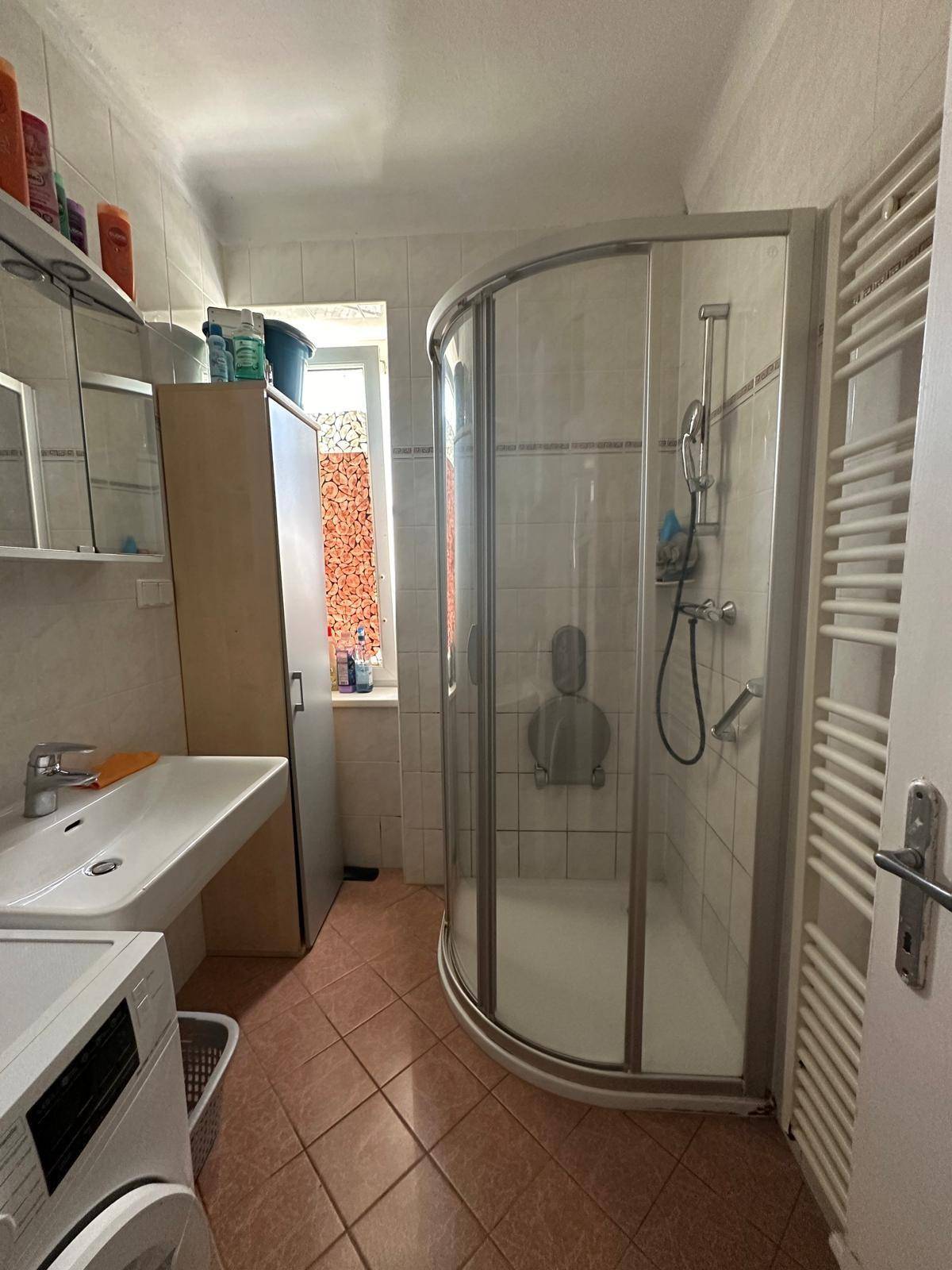 Badezimmer mit Duschkabine, Waschbecken, beheiztem Handtuchhalter und Fenster.