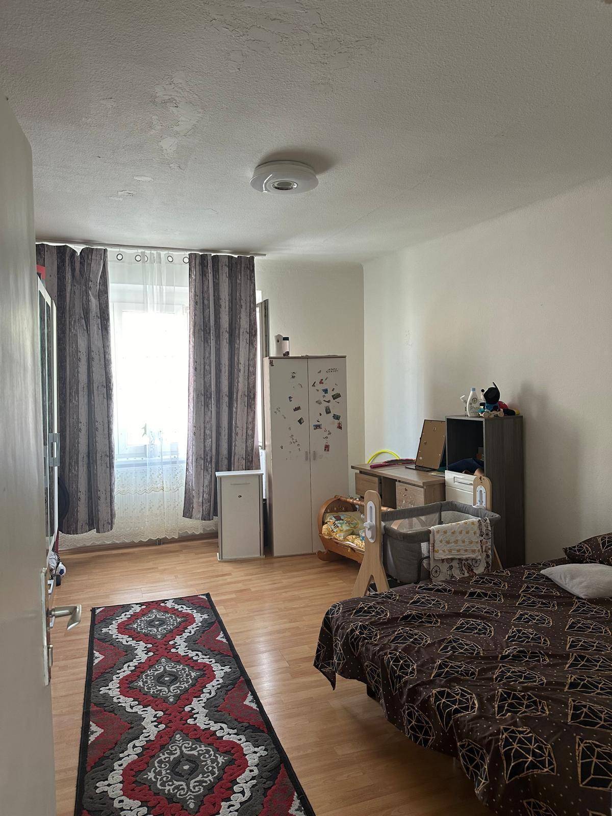Schlafzimmer mit Parkettboden, Fenster und Platz für ein Babybett, hell und freundlich.