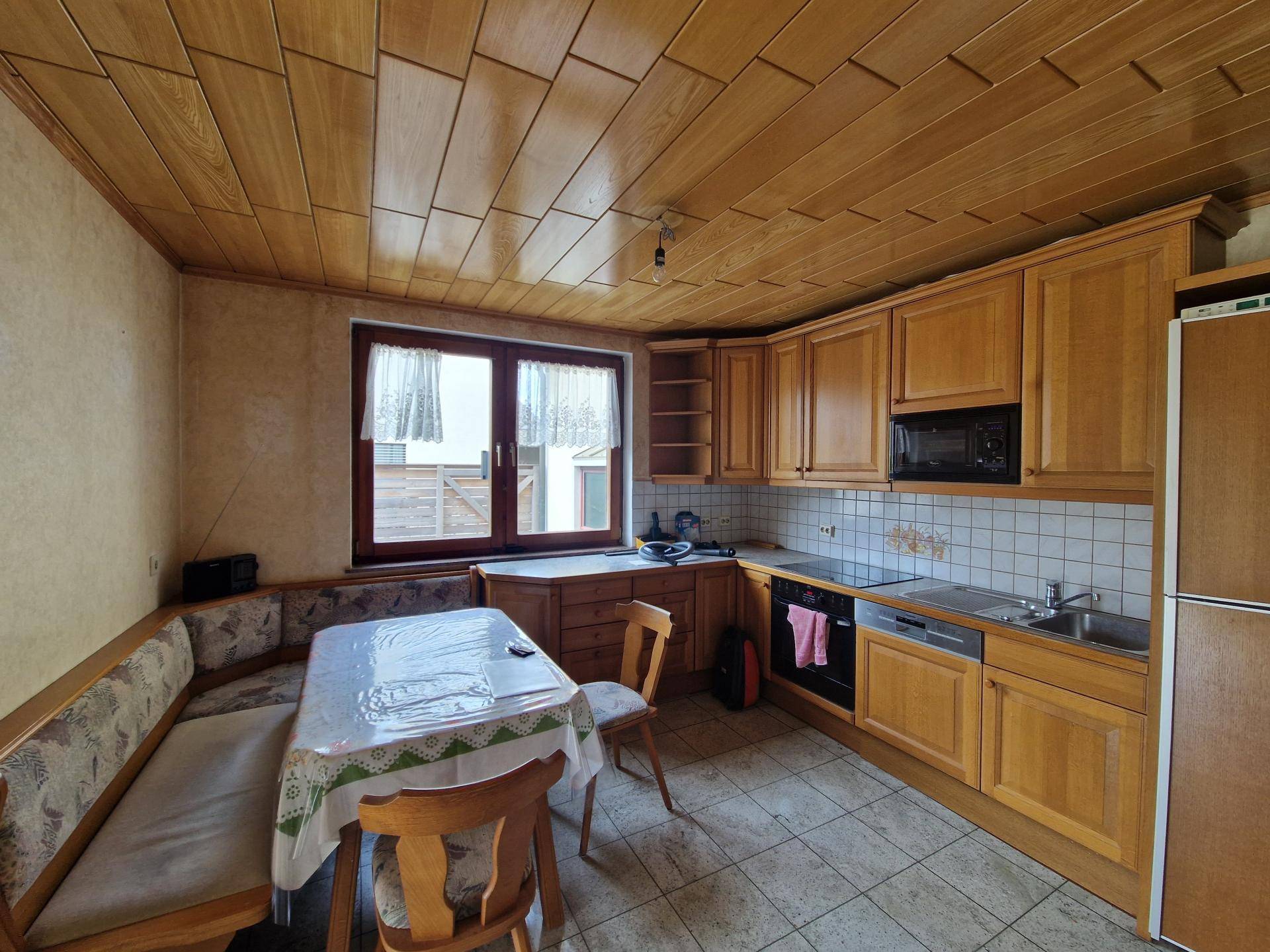 Traditionelle Küche mit Holzschränken, Essbereich und Fliesenboden in gutem Zustand.