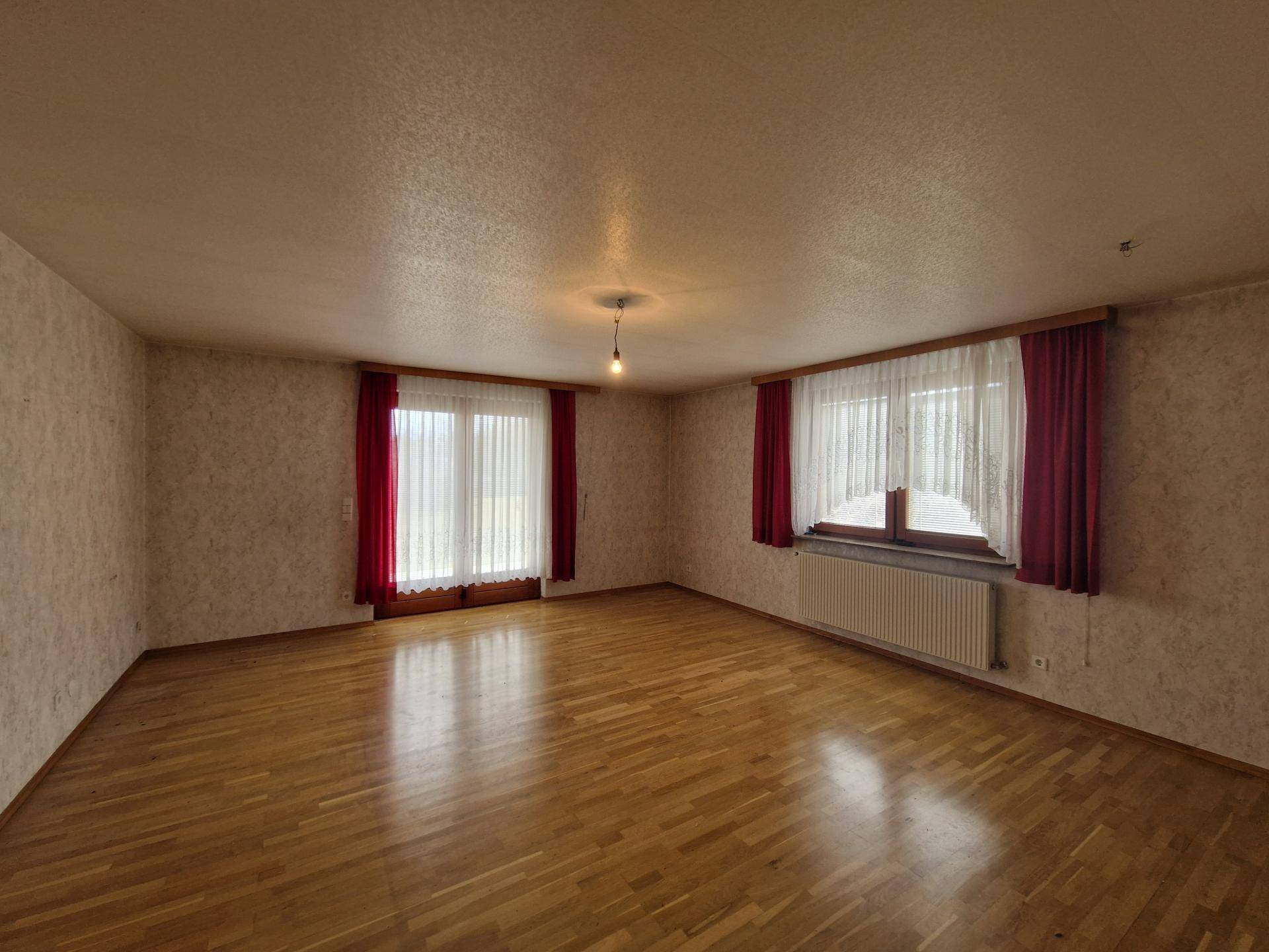 Geräumiges Wohnzimmer mit Parkettboden, großen Fenstern und Zugang zur Terrasse.