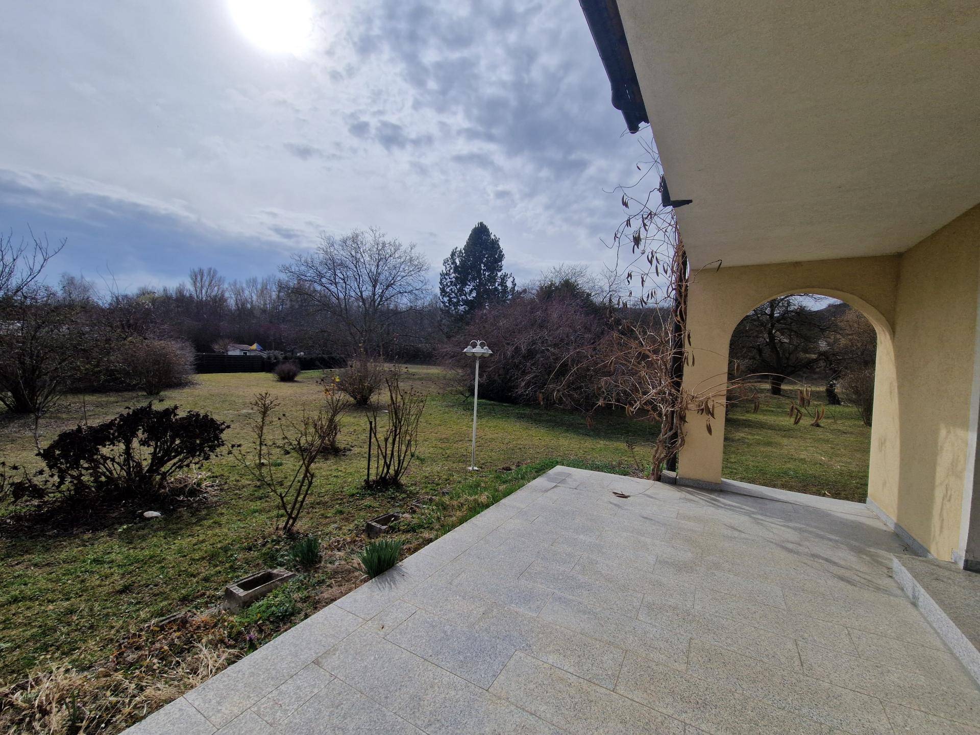 Überdachte Terrasse mit Fliesenboden und weitem Blick in den grünen Gartenbereich.