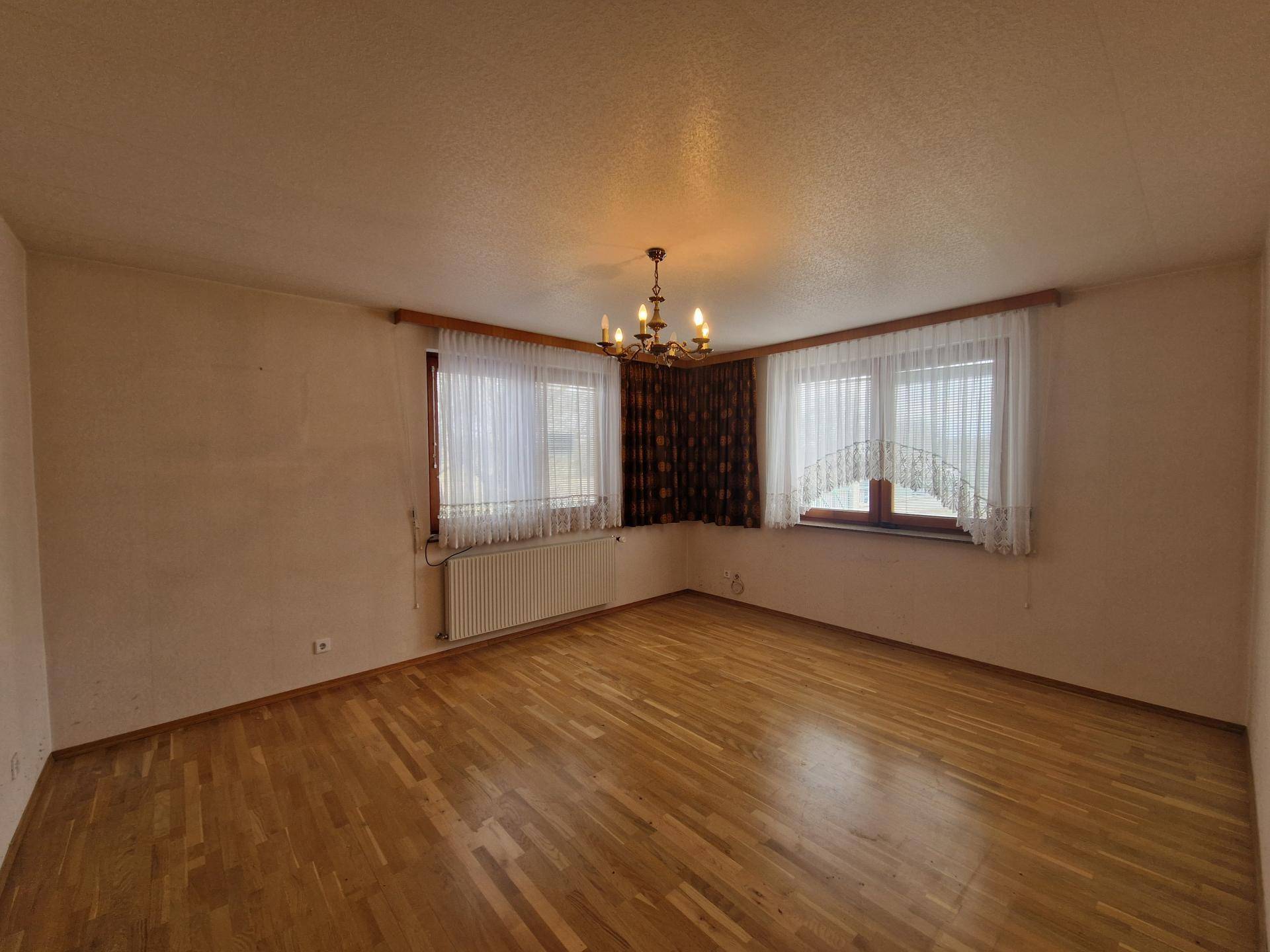 Geräumiges Wohnzimmer mit Parkettboden und zwei Fenstern für viel Tageslicht.