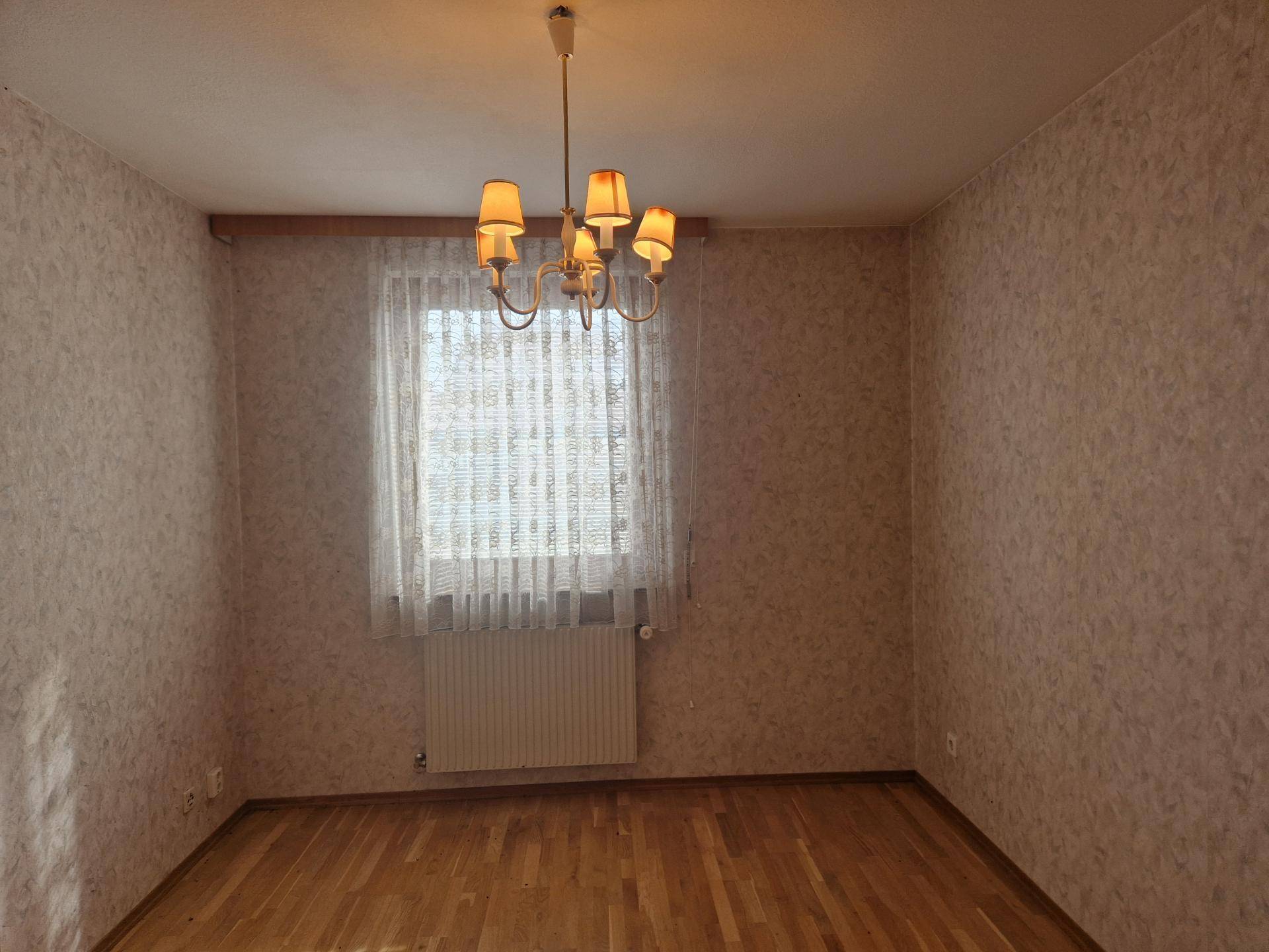 Helles Schlafzimmer mit Parkettboden und Fenster mit Blick ins Grüne.