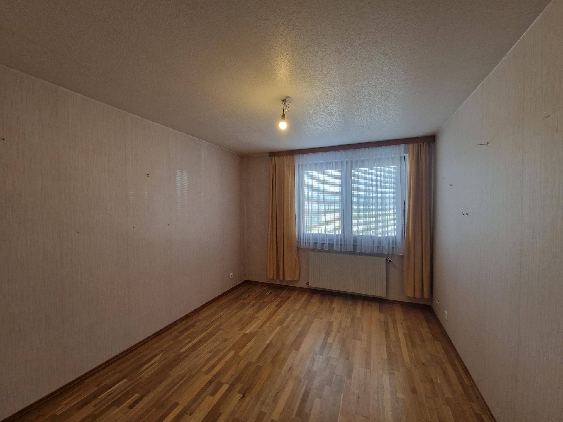 Helles Schlafzimmer mit Parkettboden und Fenster mit gelben Vorhängen.