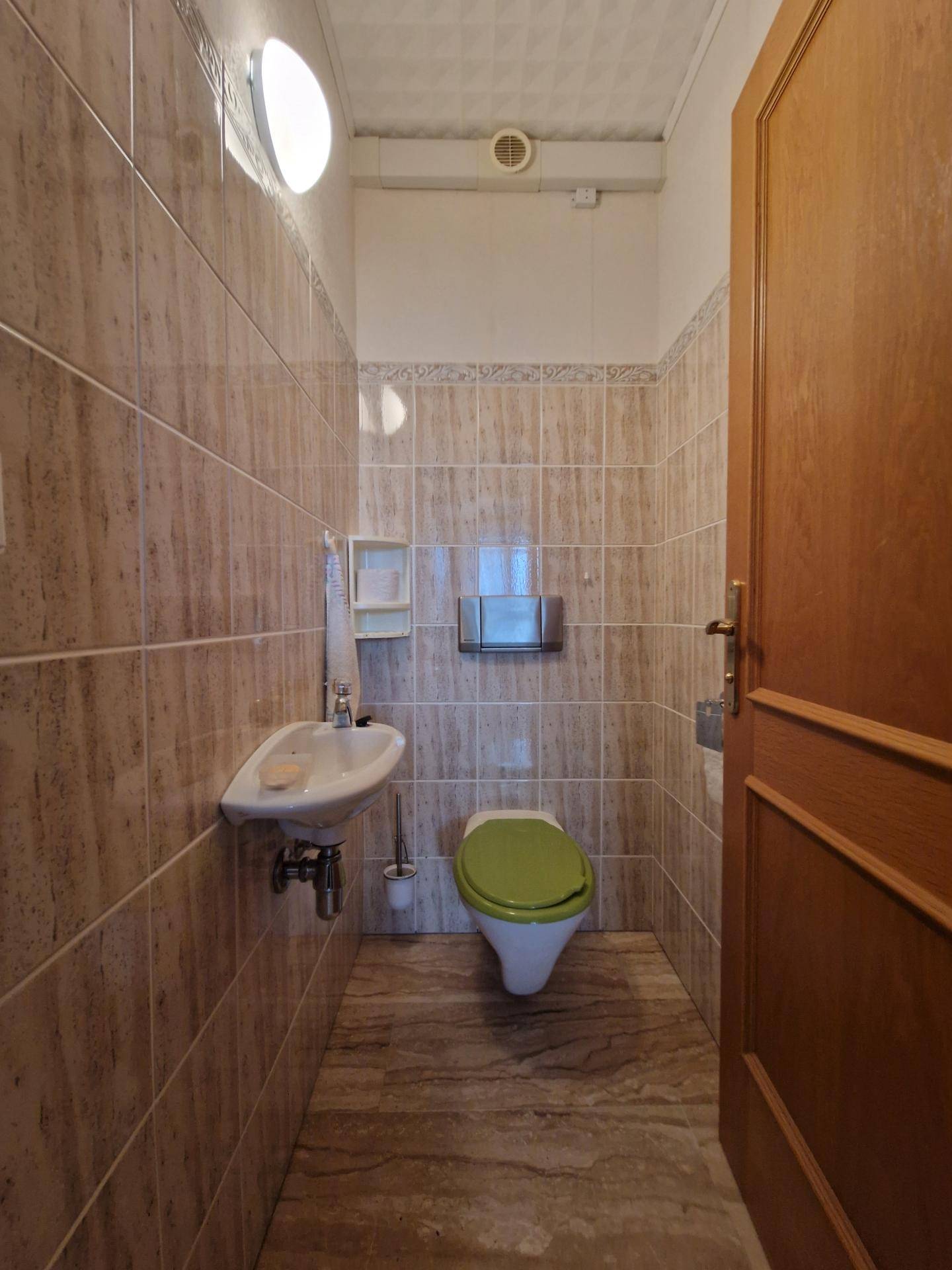Separate Toilette mit Waschbecken und Fliesen an Wänden und Boden.