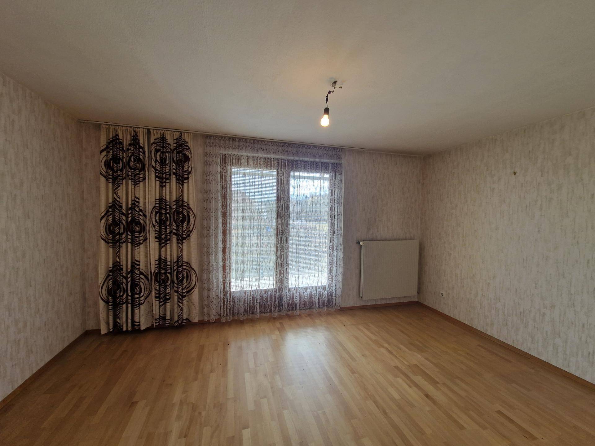 Helles Wohnzimmer mit Parkettboden und Zugang zu einem Balkon oder einer Terrasse.