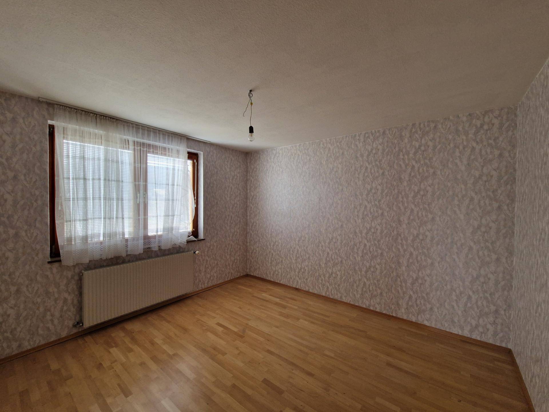 Schlafzimmer mit Parkettboden und Fenster mit Blick ins Grüne.