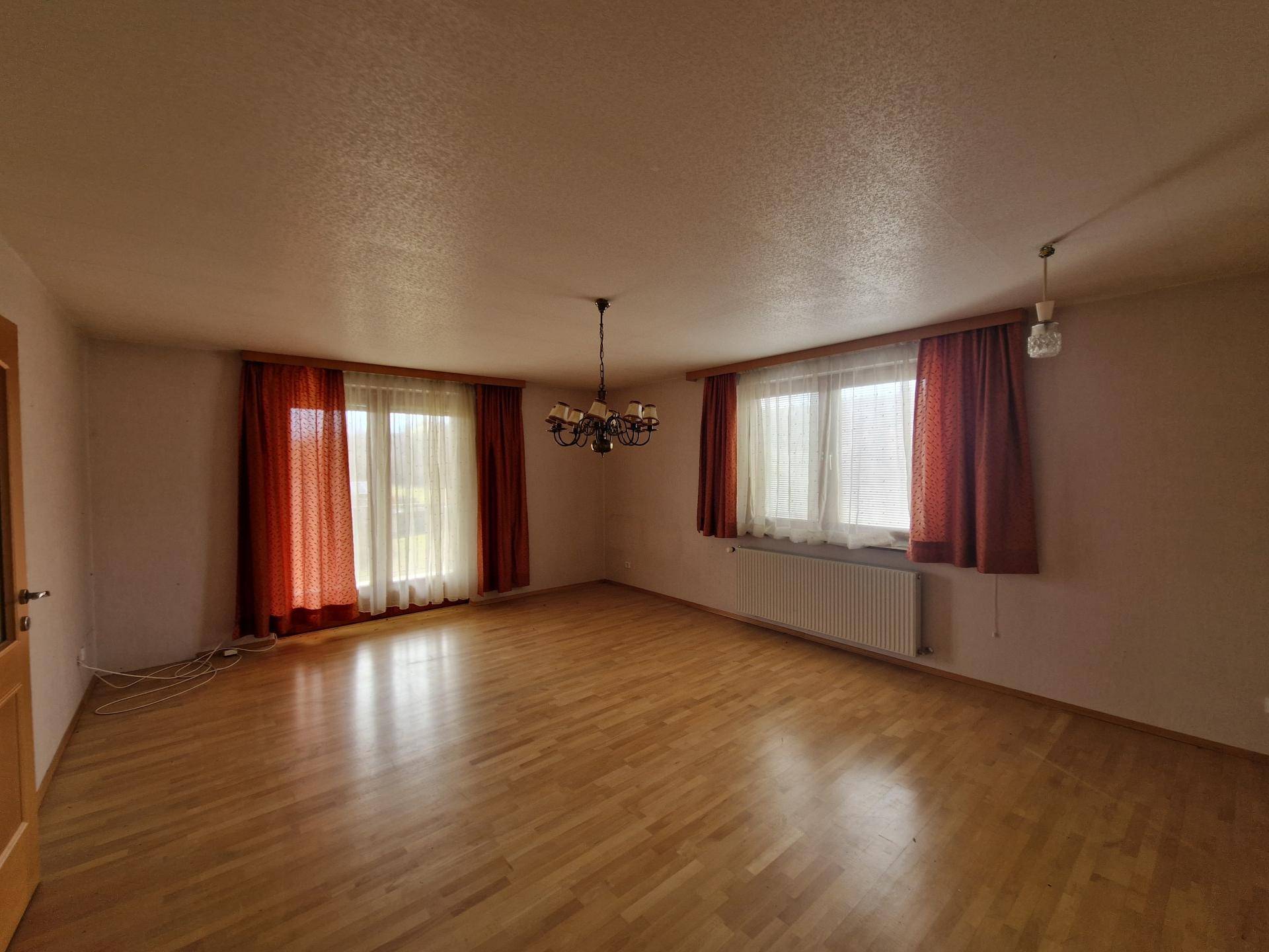 Geräumiges Wohnzimmer mit Parkettboden und zwei Fenstern für viel Tageslicht.