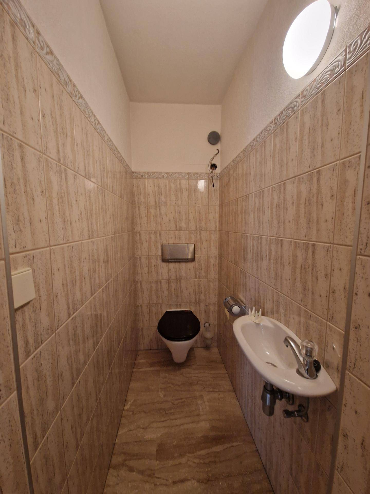 Separate Toilette mit Waschbecken und Fliesen an Wänden und Boden.