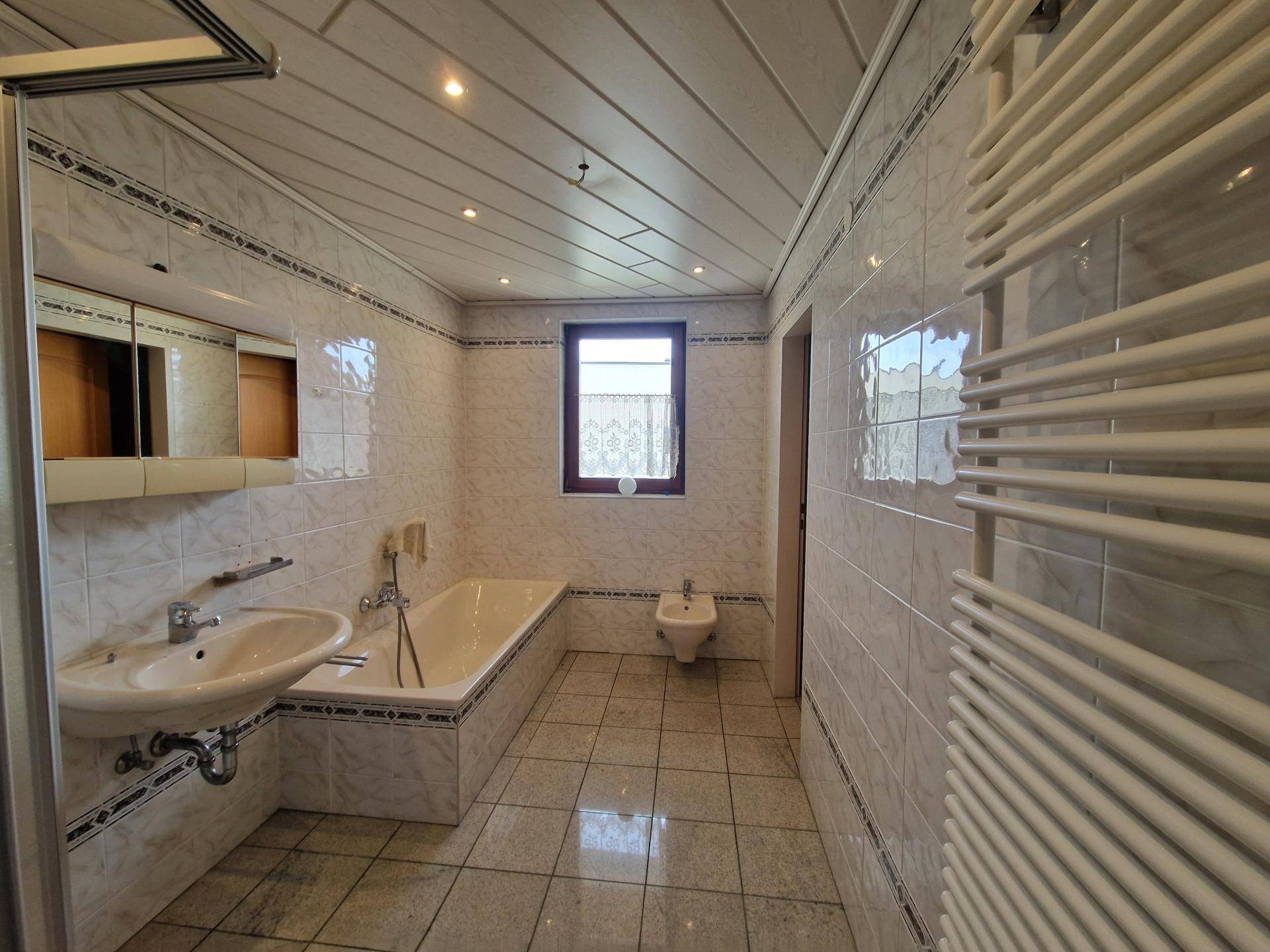 Gefliestes Badezimmer mit Badewanne, Bidet, Einzelwaschbecken und Handtuchheizkörper.