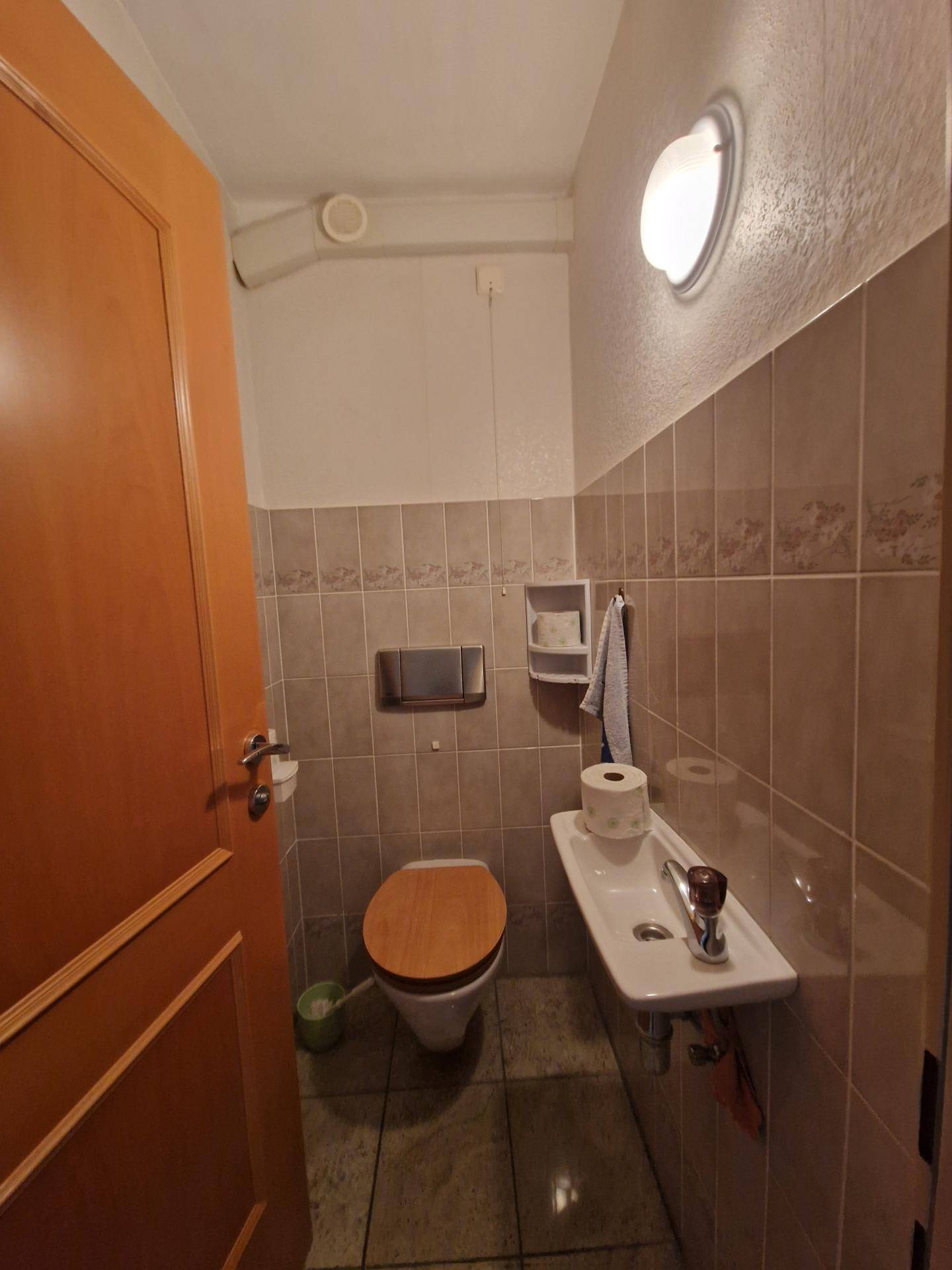 Separate Toilette mit Waschbecken und Fliesen an Wänden und Boden.