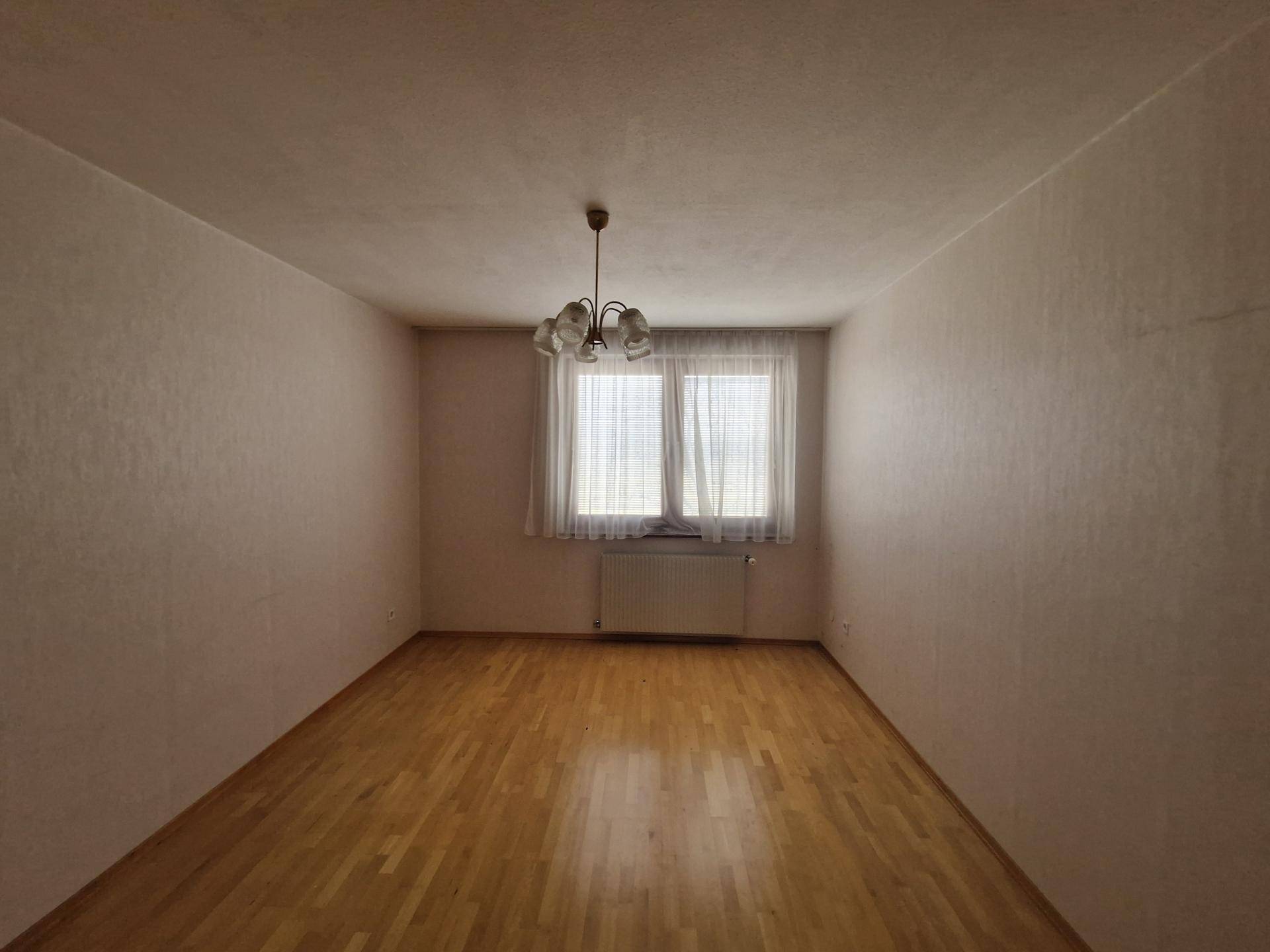 Schlafzimmer mit Parkettboden und Fenster mit Blick auf die Umgebung.