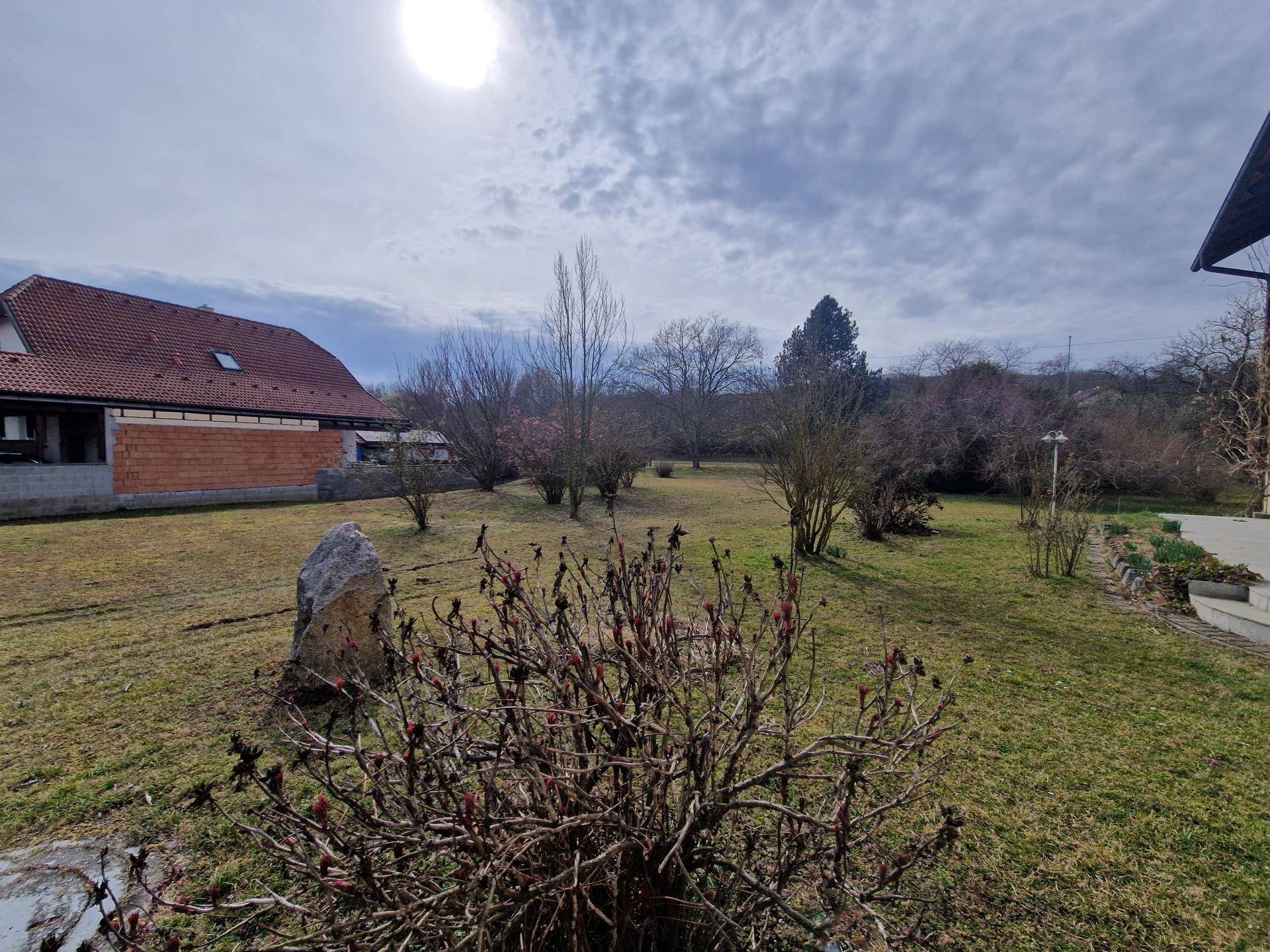 Großer Gartenbereich mit Rasenfläche, Sträuchern und einem dekorativen Felsen.