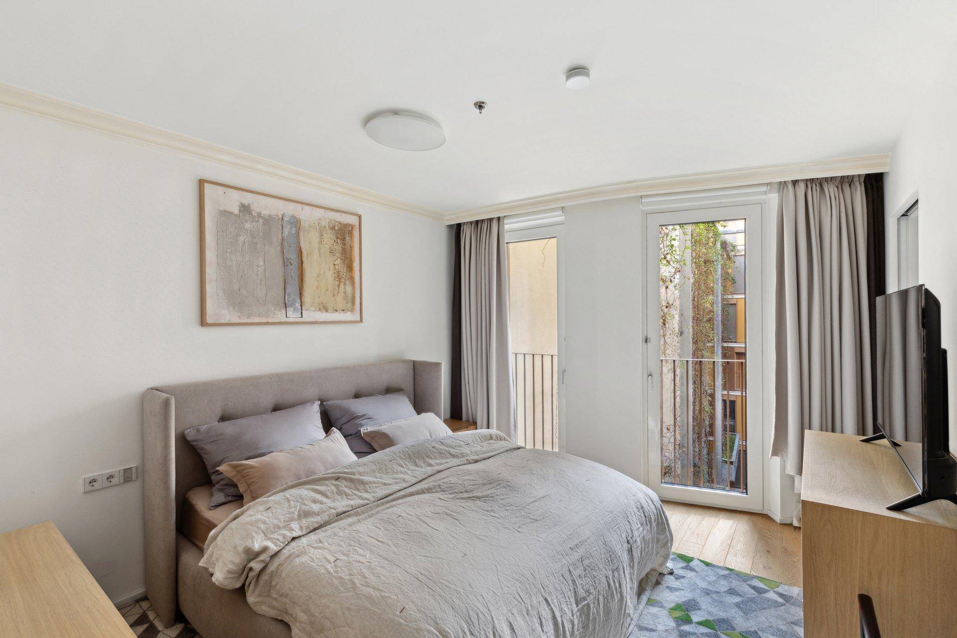 Gemütliches Schlafzimmer mit Doppelbett, Holzboden und Zugang zu einem französischen Balkon.