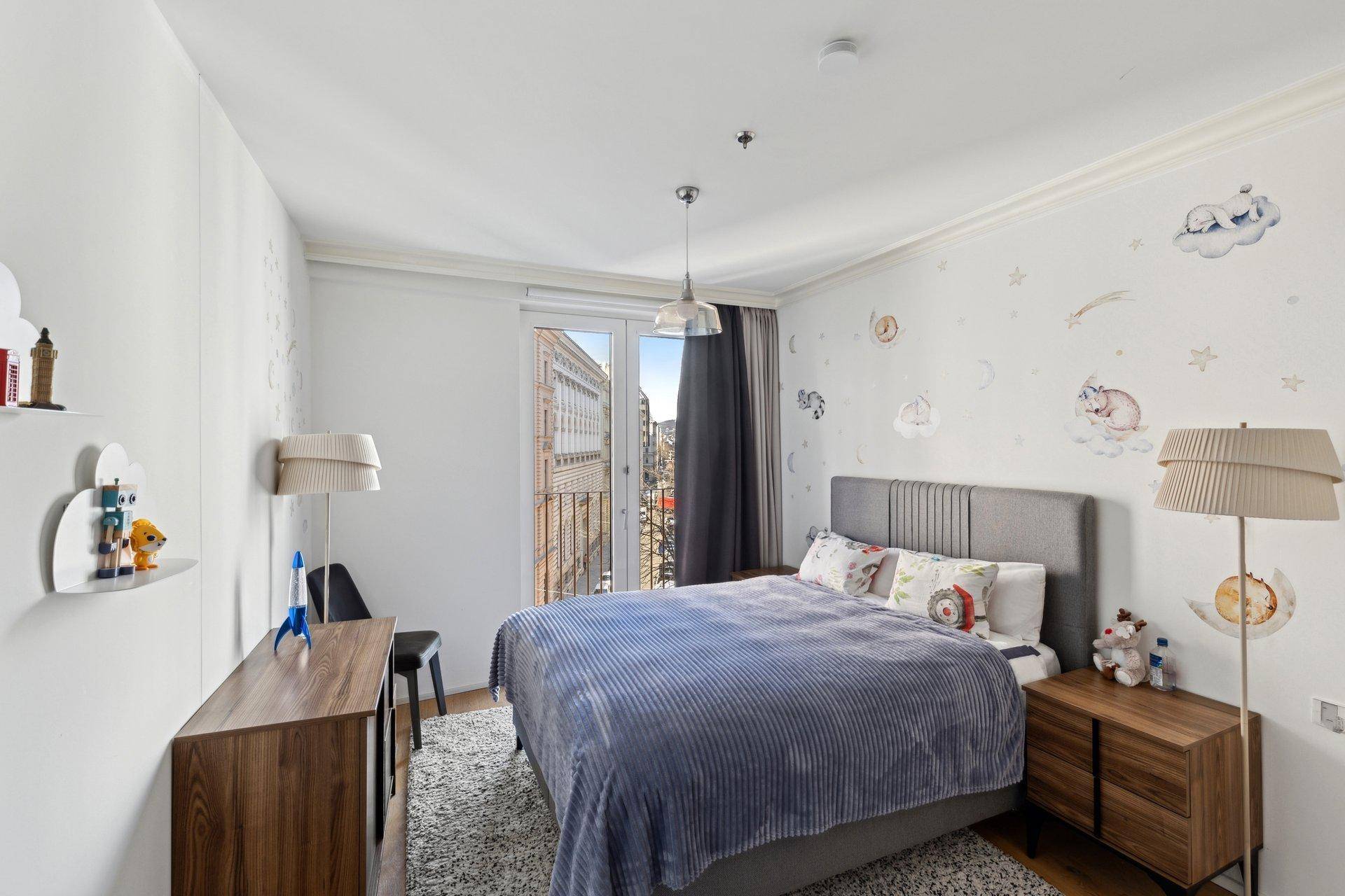 Kinderzimmer mit Einzelbett, verspielter Wanddekoration und Zugang zu einem französischen Balkon.