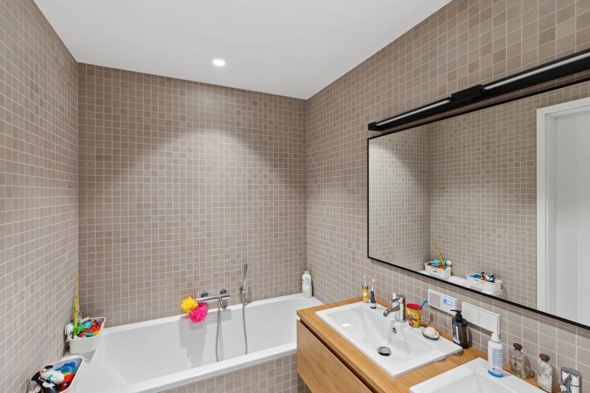 Badezimmer mit Badewanne, Doppelwaschbecken und beigefarbenen Mosaikfliesen.